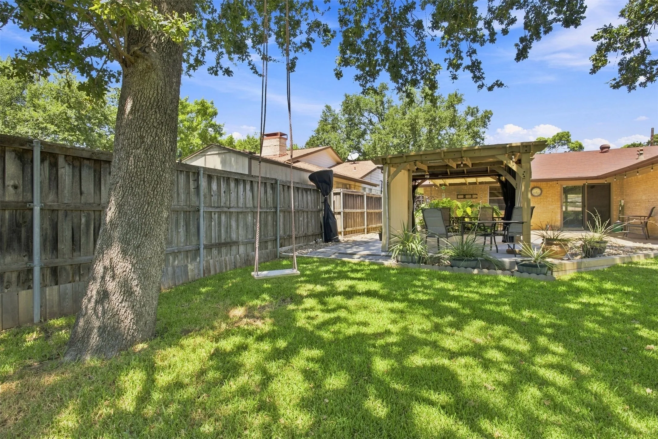 Expansive backyard featuring a manicured lawn, a built-in wooden pergola, swing, and a privacy fence