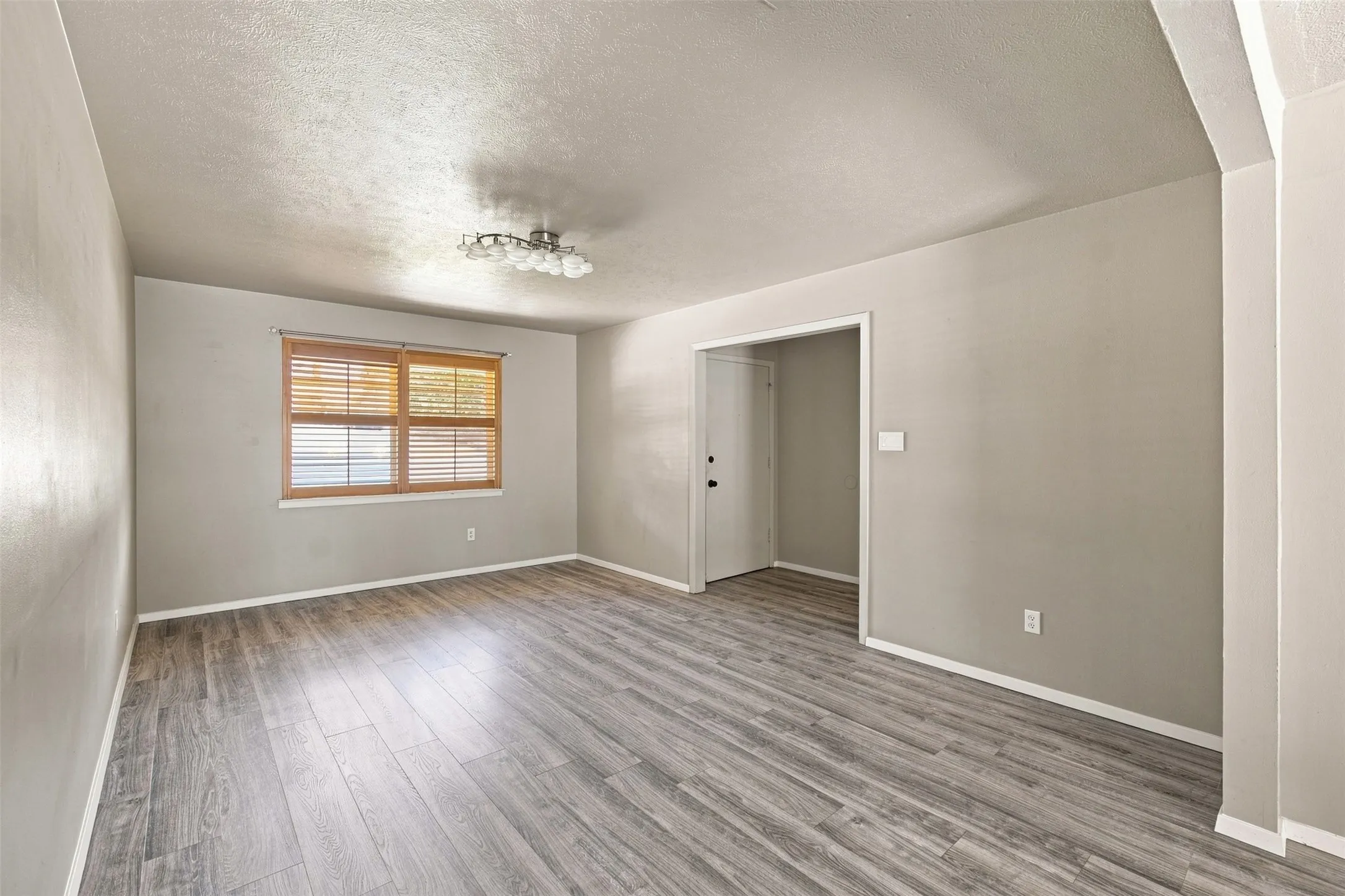 Wood-finish flooring, neutral wall tones, window with natural wood blinds, contemporary ceiling light fixture, and white trim throughout