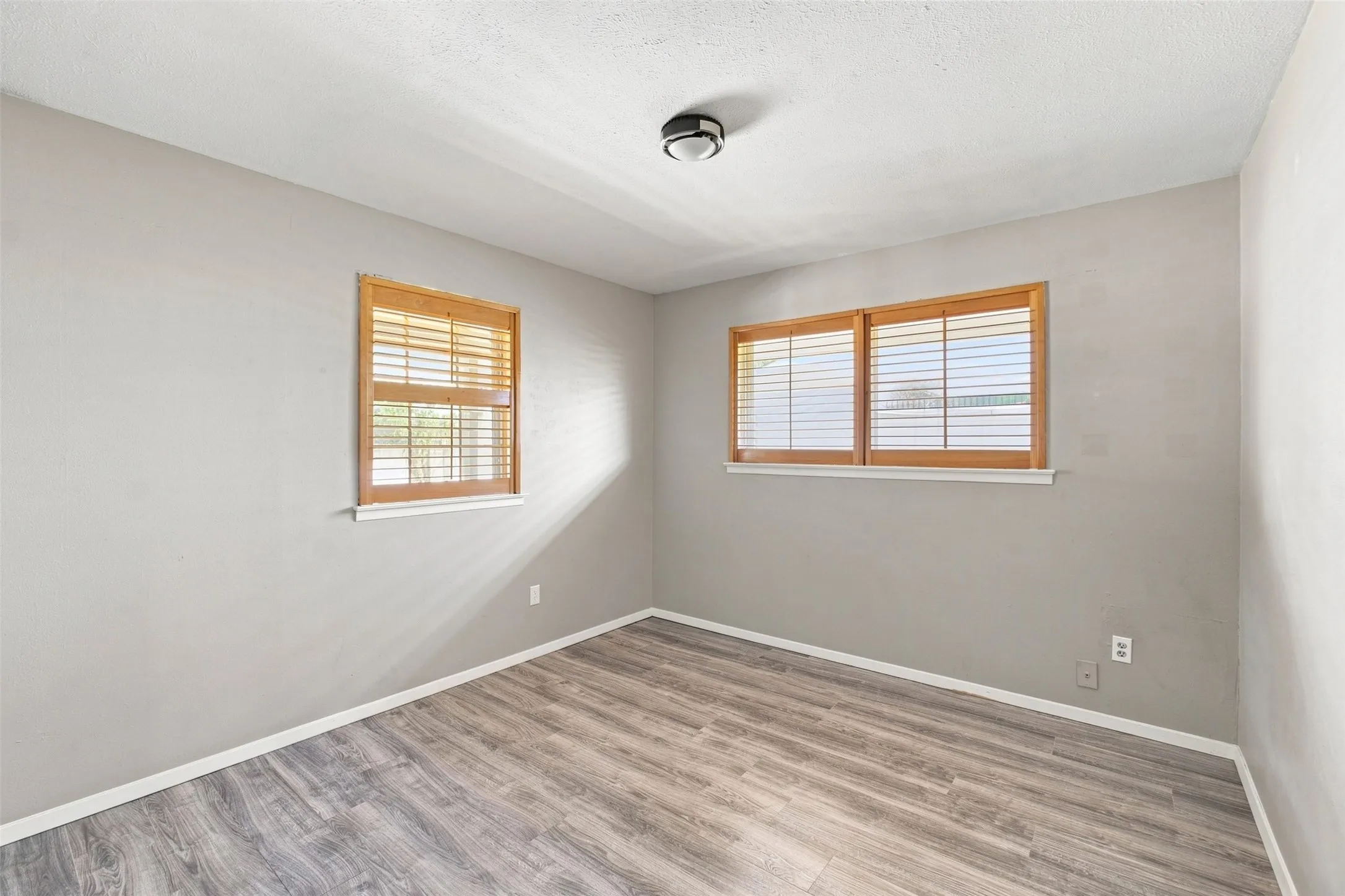 Wood-finish flooring, neutral wall tones, two windows with wood blinds, and a flush mount ceiling light