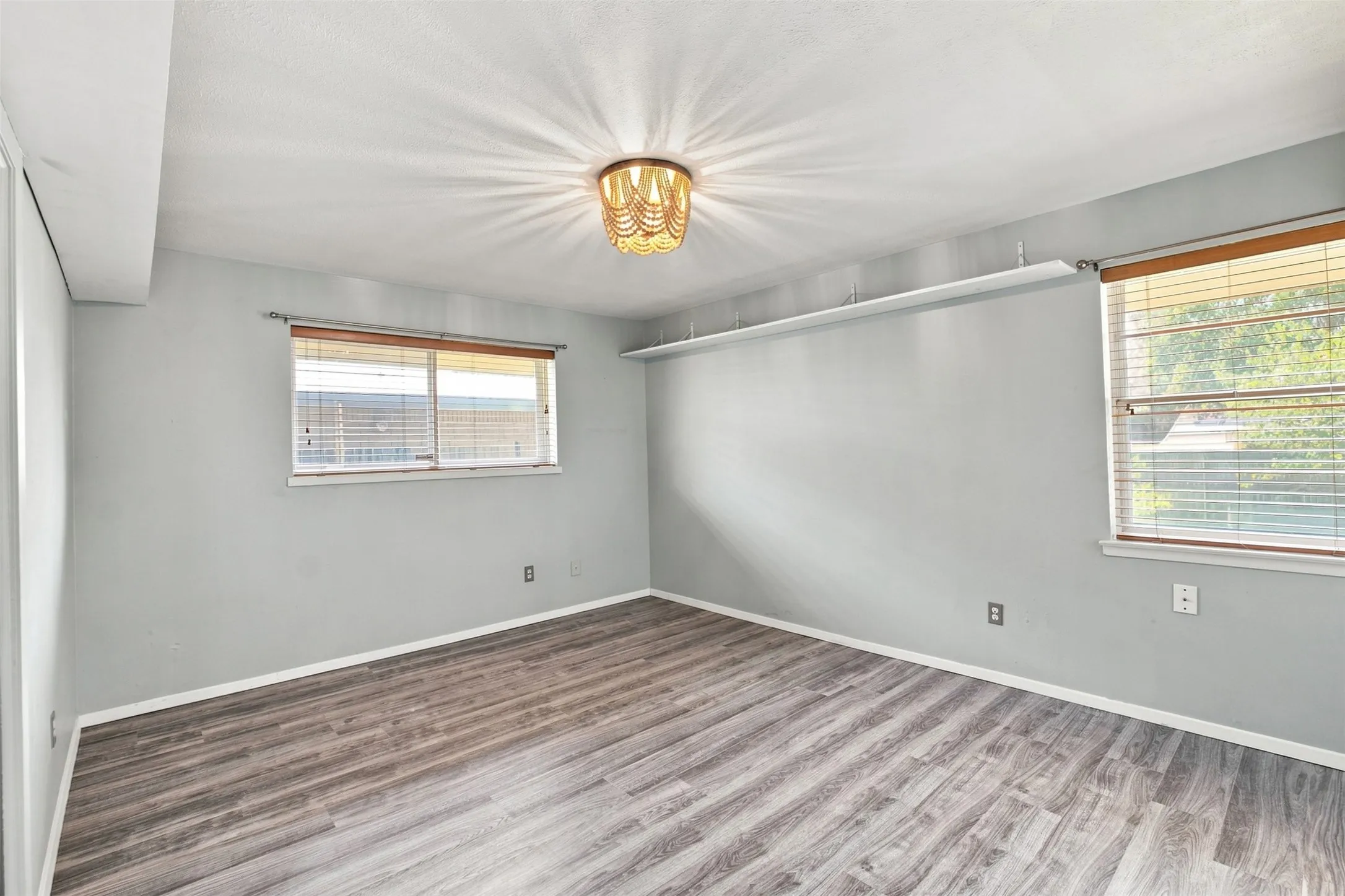 Spacious primary bedroom featuring updates flooring, abundant natural light  and a distinctive light fixture.