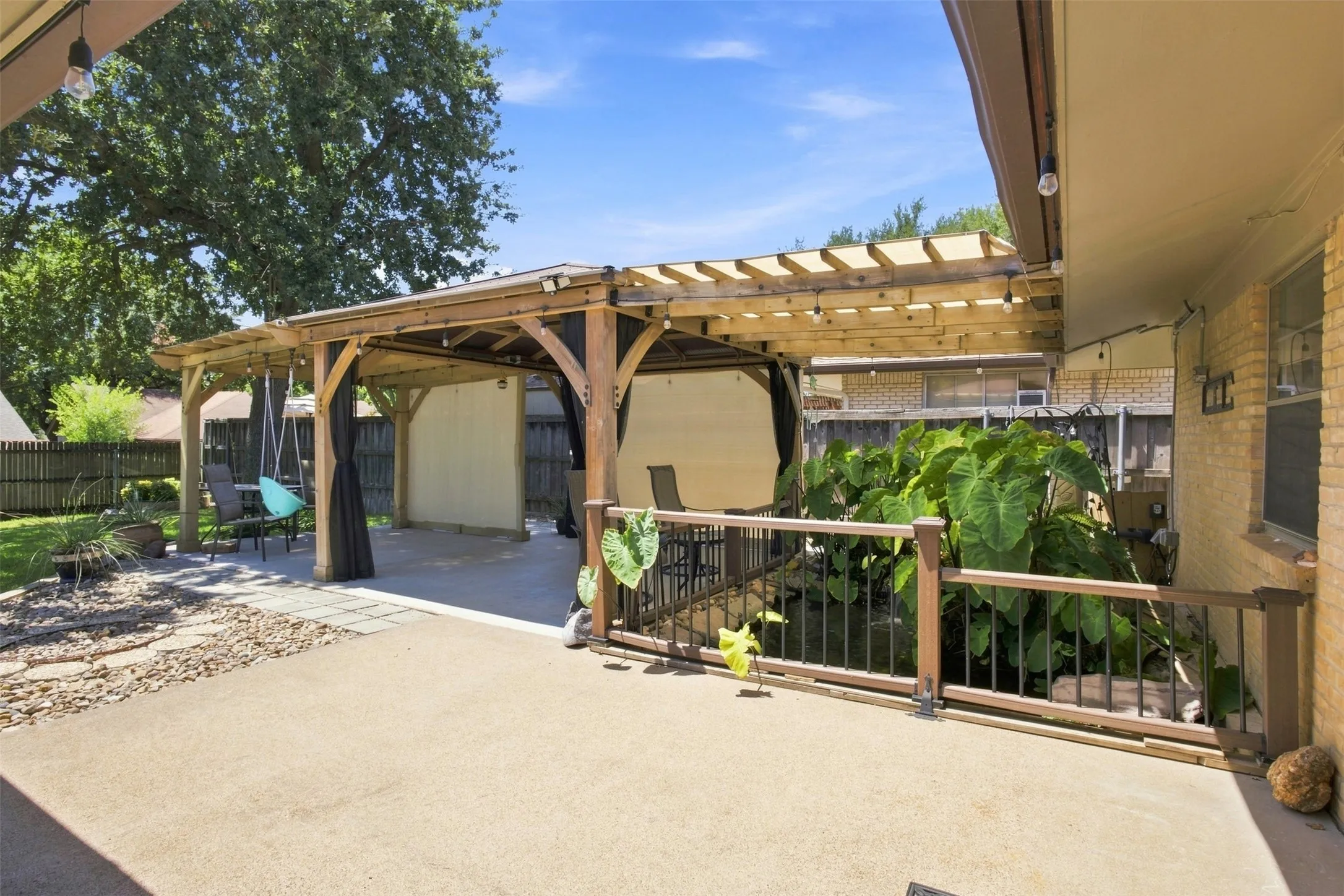 Expansive concrete patio with a wooden pergola featuring a retractable canopy, decorative pond, integrated lighting, and privacy screens