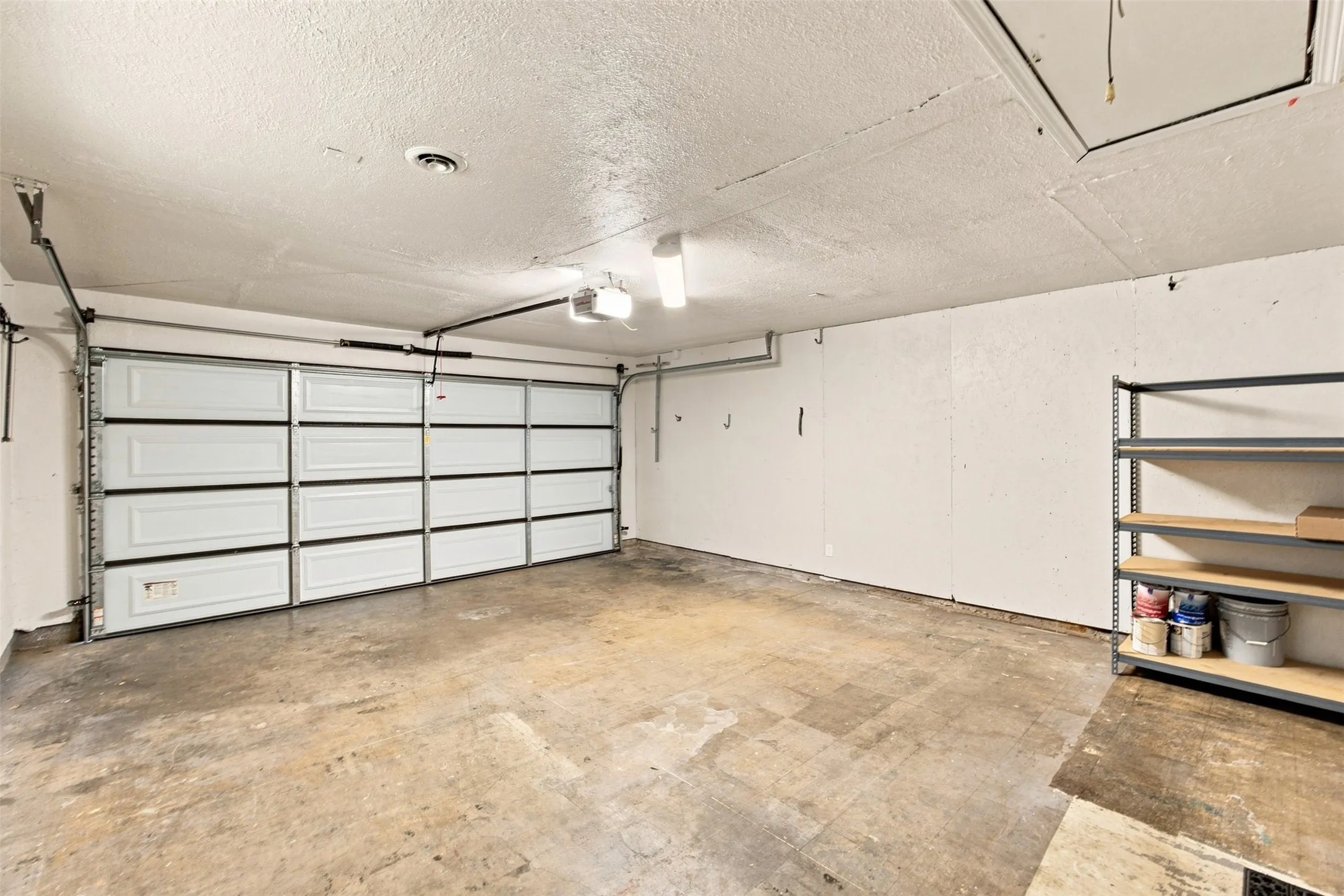 Spacious garage featuring a paneled overhead door, concrete flooring, overhead lighting, and shelving