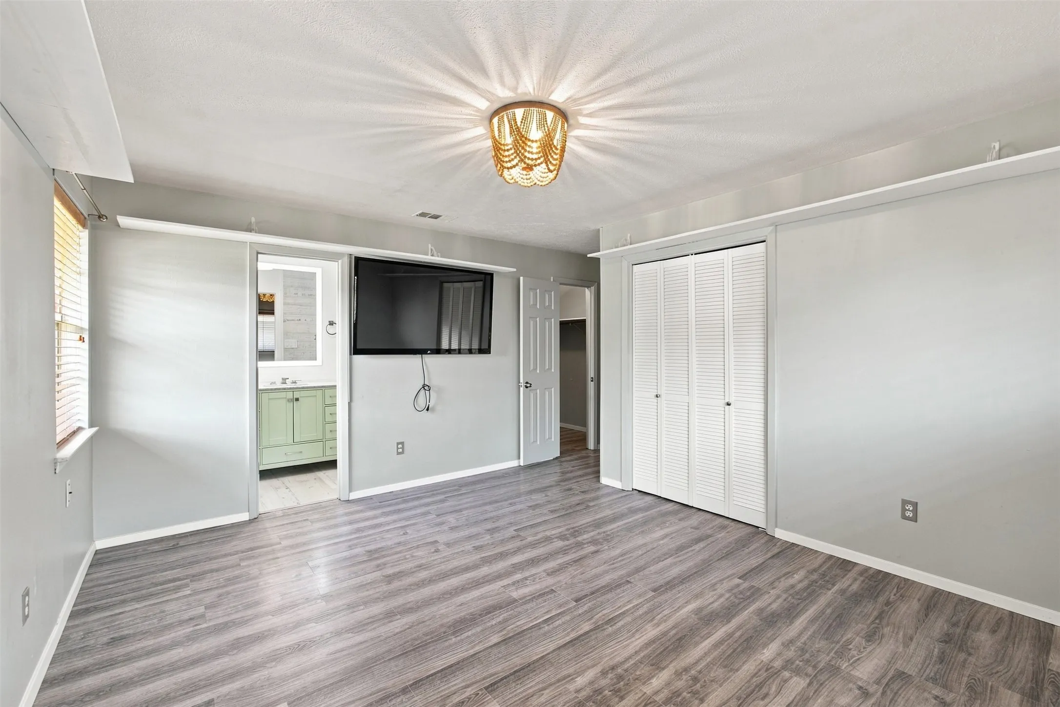 Primary bedroom with updated flooring, statement light fixture, and direct access to the ensuite bath.