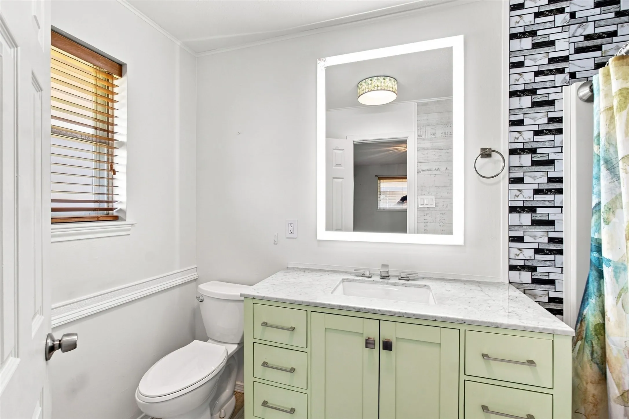 Bathroom vanity with a white countertop and integrated sink, illuminated mirror, and a decorative tiled wall