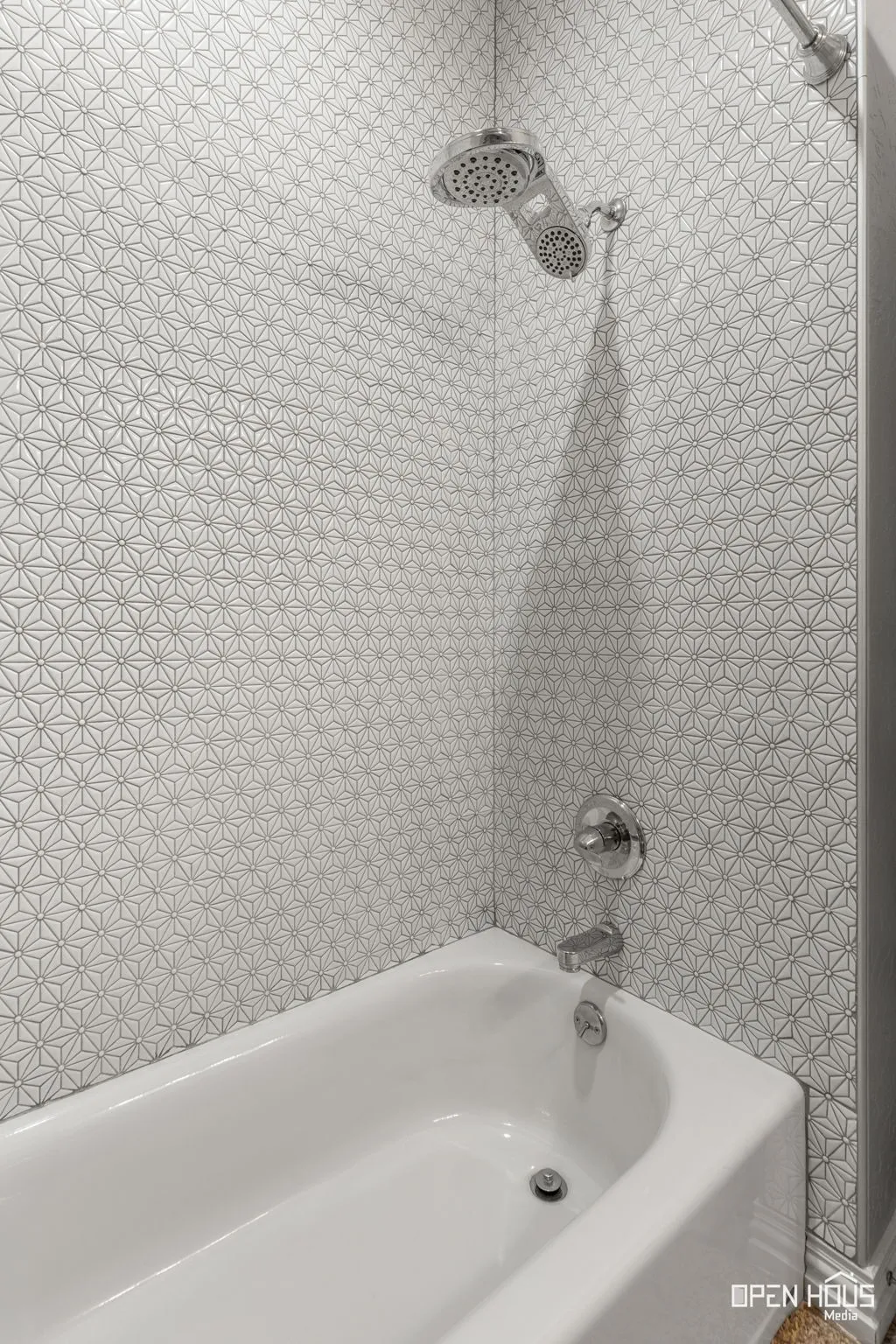 Bathtub and shower combination with chrome fixtures and patterned tile surround