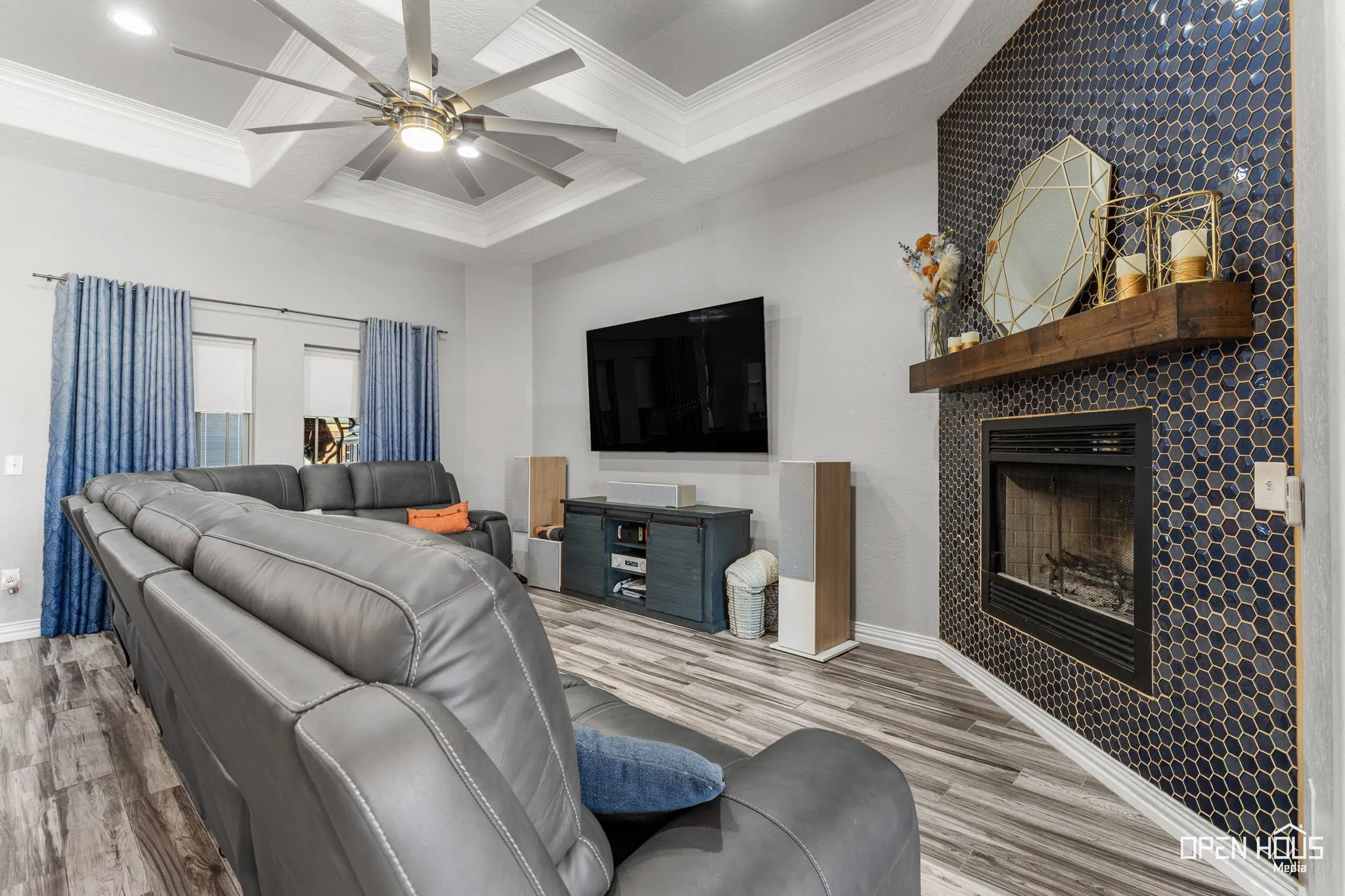Tray ceiling with crown molding, ceiling fan, wood-finish flooring, built-in fireplace with a wood mantle, and mosaic tile surround