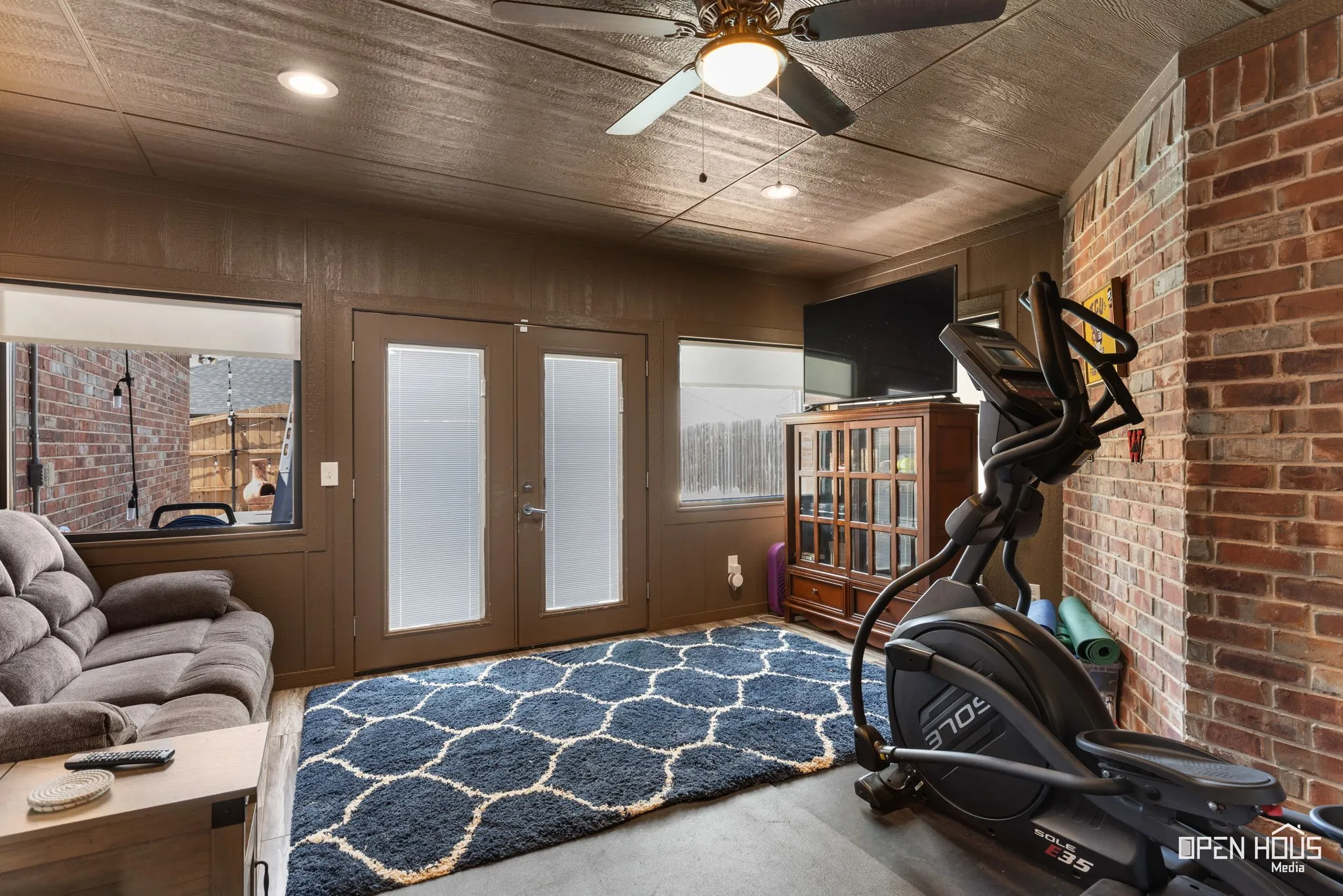 Enclosed patio space featuring exposed brick, wood paneling, dual glass-paneled French doors, and a ceiling fan with integrated lighting