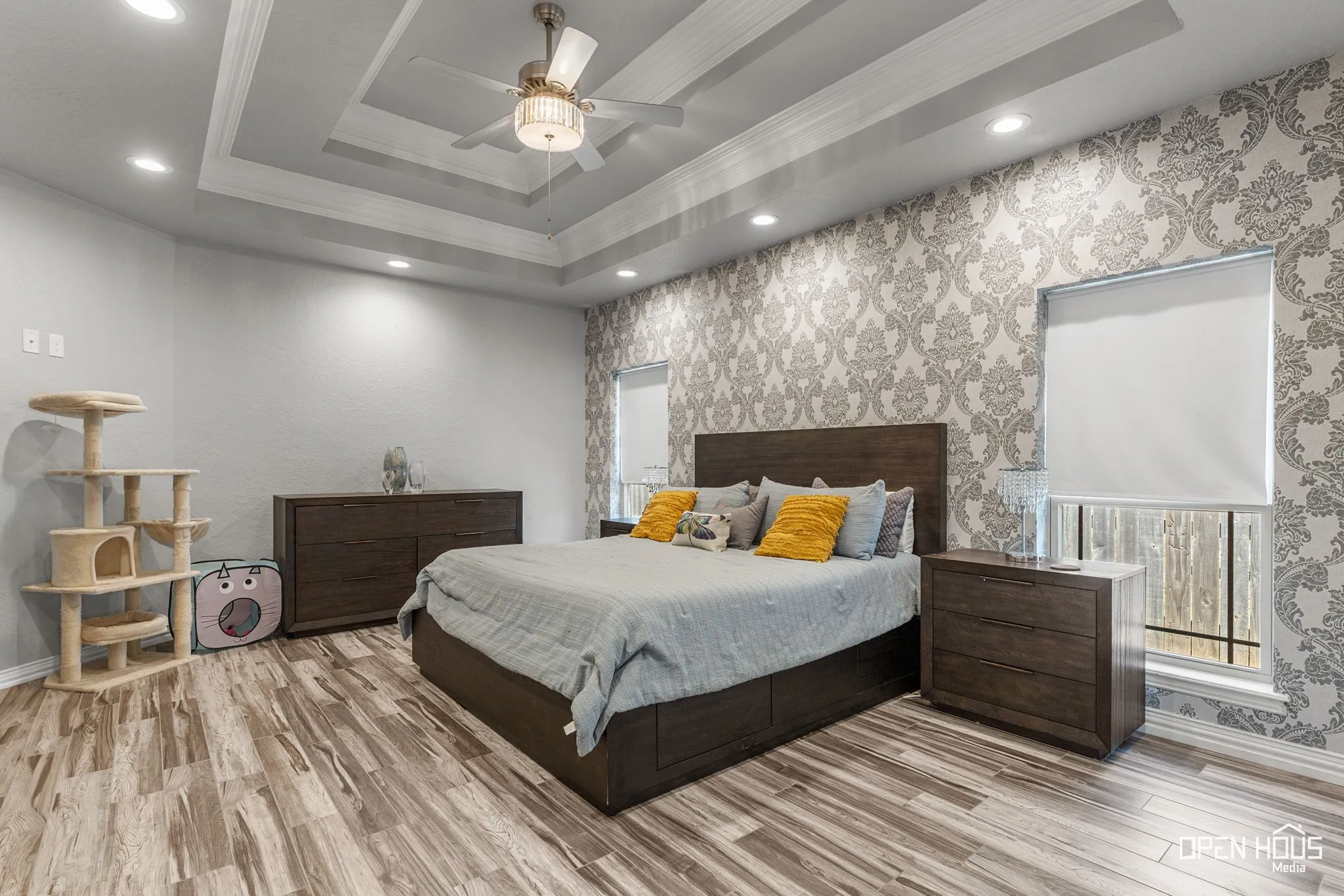 Tray ceiling with recessed lighting and a ceiling fan, accent wall with patterned wallpaper, tile flooring, and windows with roller shades