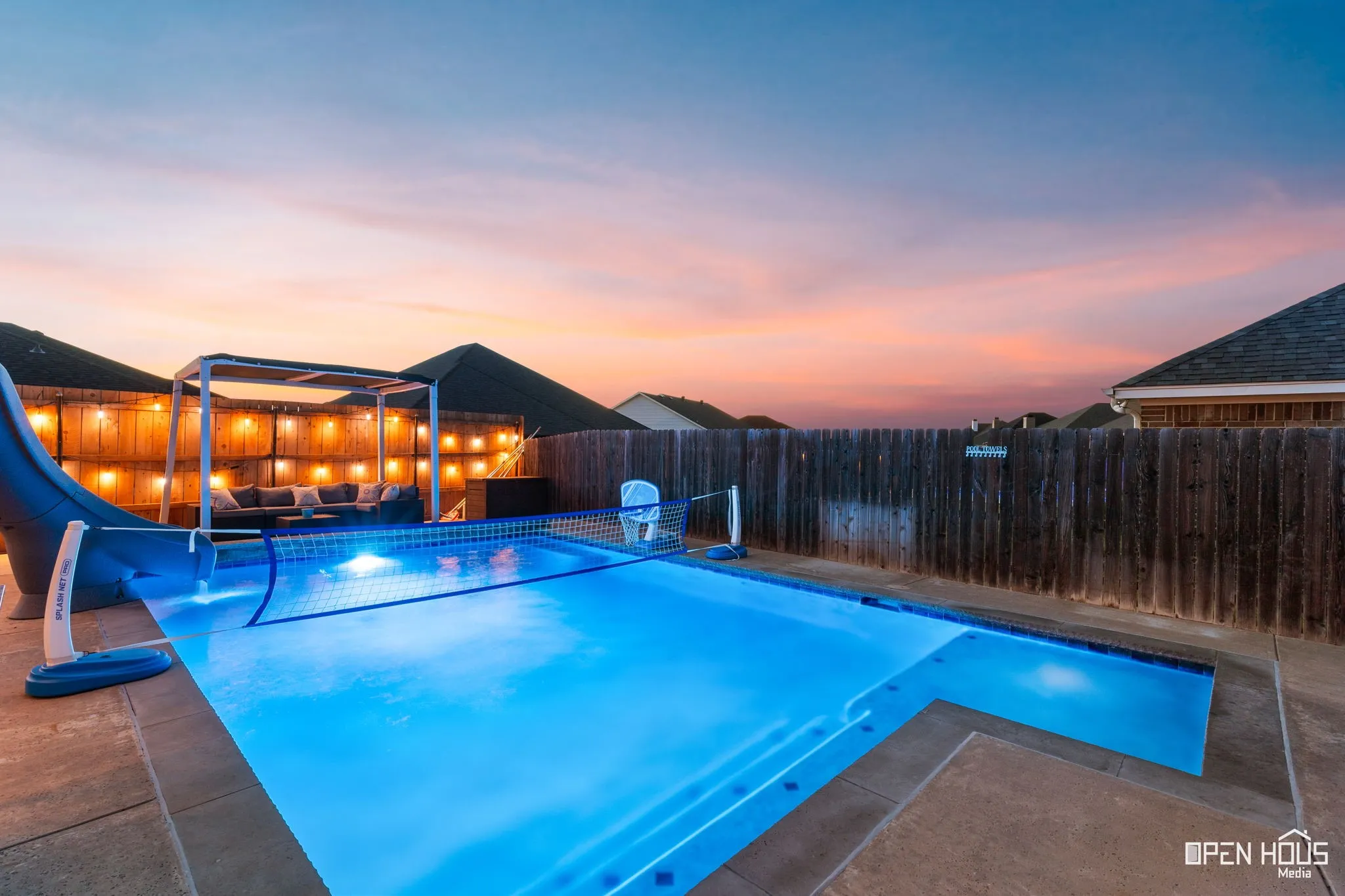 In-ground swimming pool with integrated steps, surrounding concrete decking, a privacy fence, and an outdoor pergola