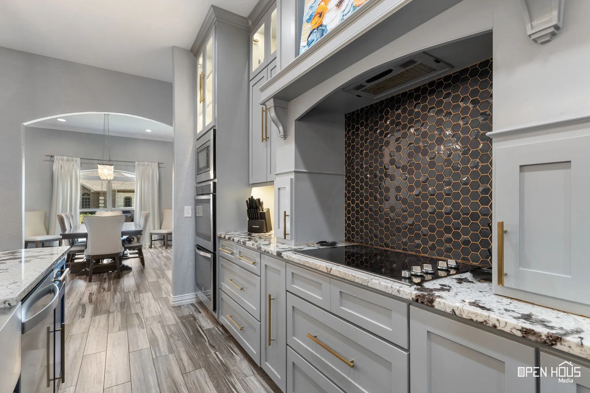 Light gray cabinetry with gold-tone hardware, built-in double ovens, and a black hexagonal tile backsplash