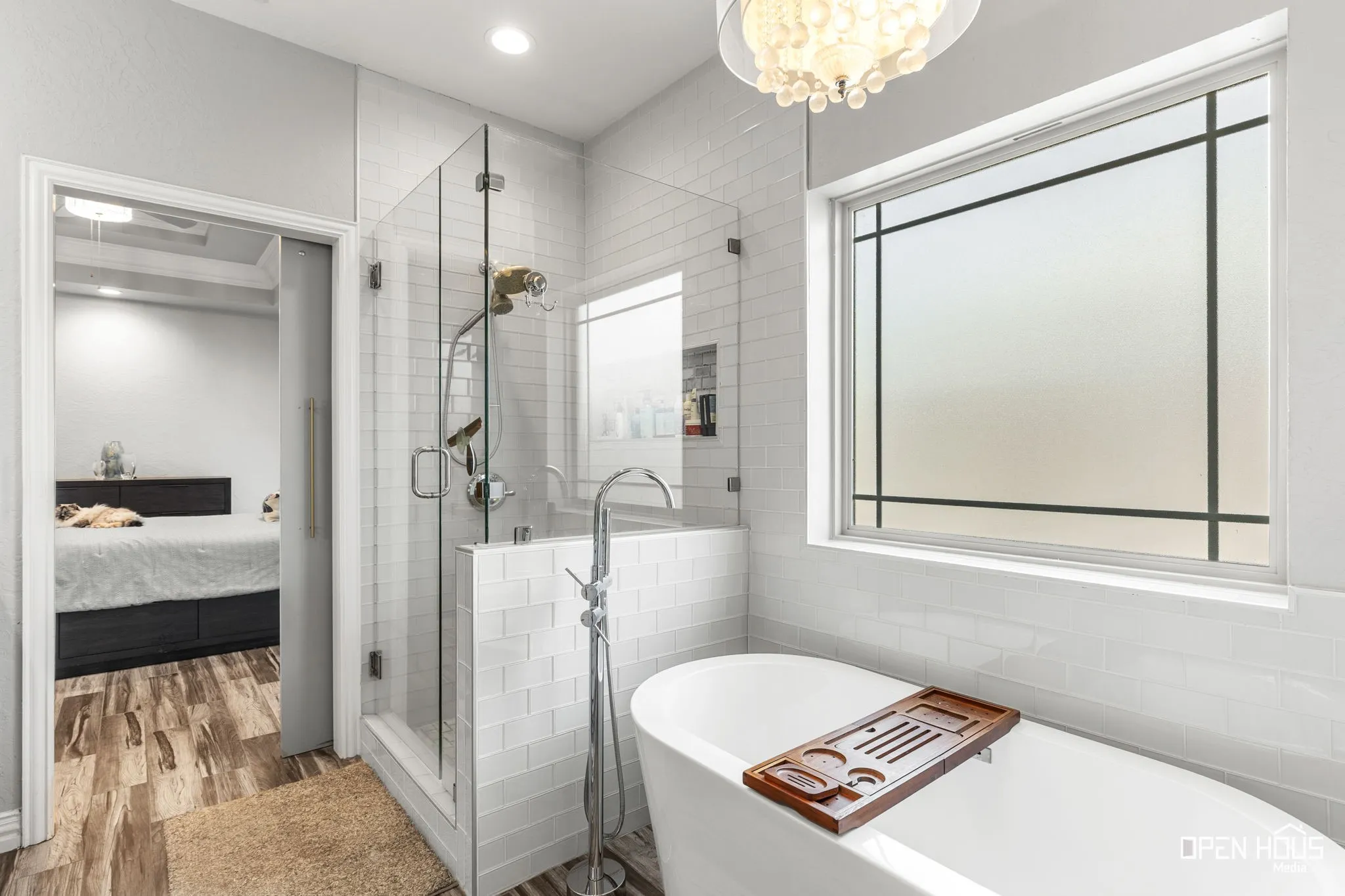 Freestanding soaking tub with floor-mounted faucet, glass-enclosed shower with tile surround, and large window with decorative mullions