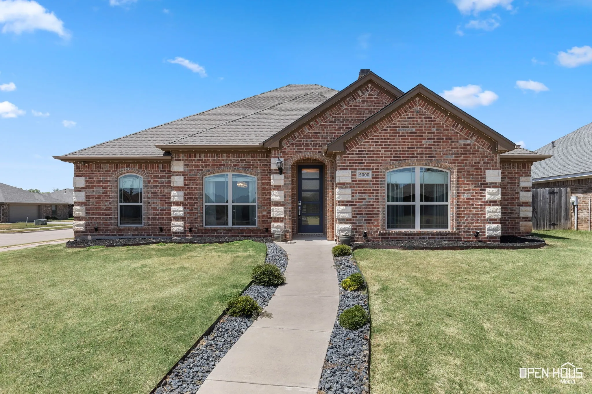 Brick exterior with stone accents, arched windows, and a paved walkway with decorative rock landscaping