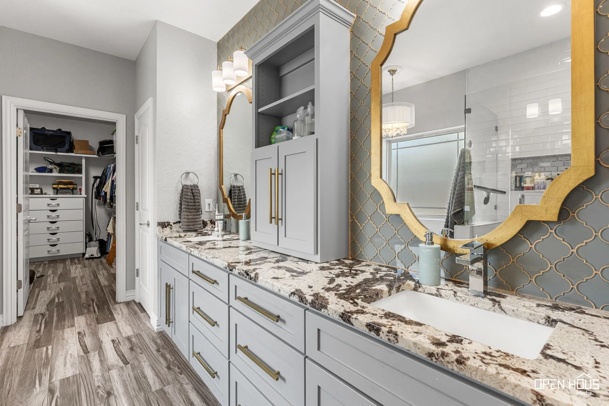 Dual vanity with integrated sinks, light gray cabinetry with gold-tone hardware, and a patterned tile backsplash