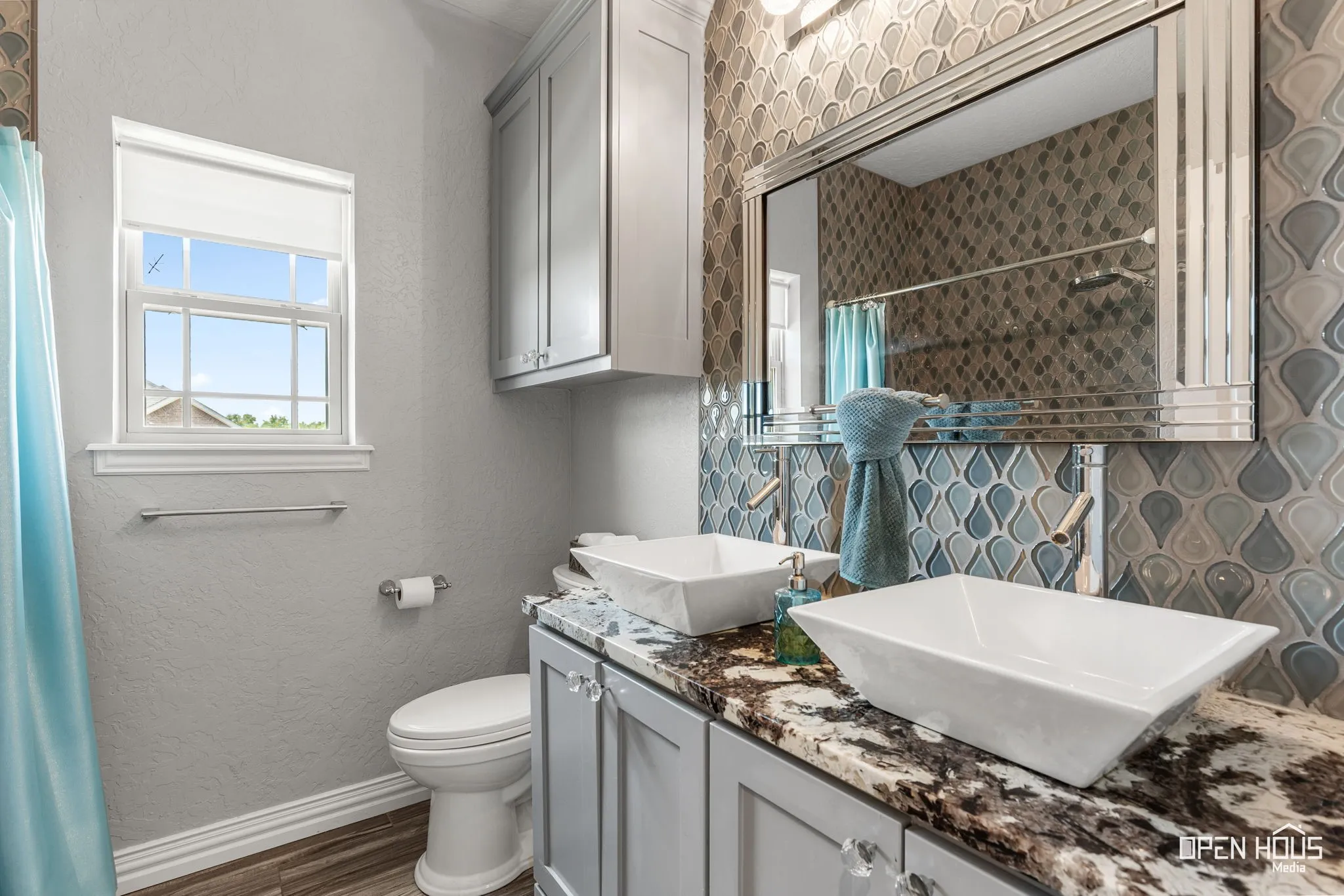 Dual vessel sinks set on a granite-finish countertop, complemented by a mosaic tile backsplash