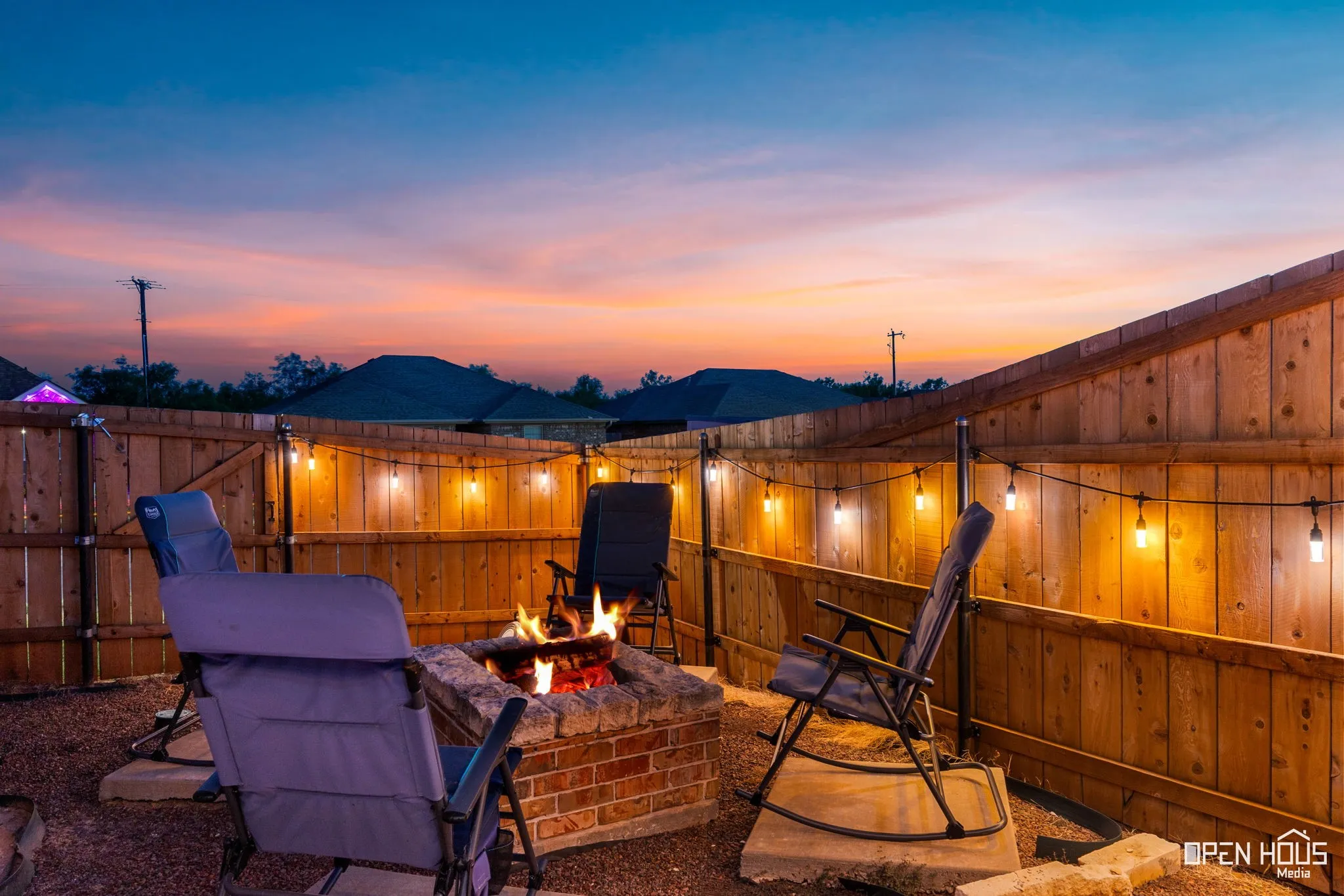 Private backyard with a brick and stone fire pit, string lighting, and wood fencing