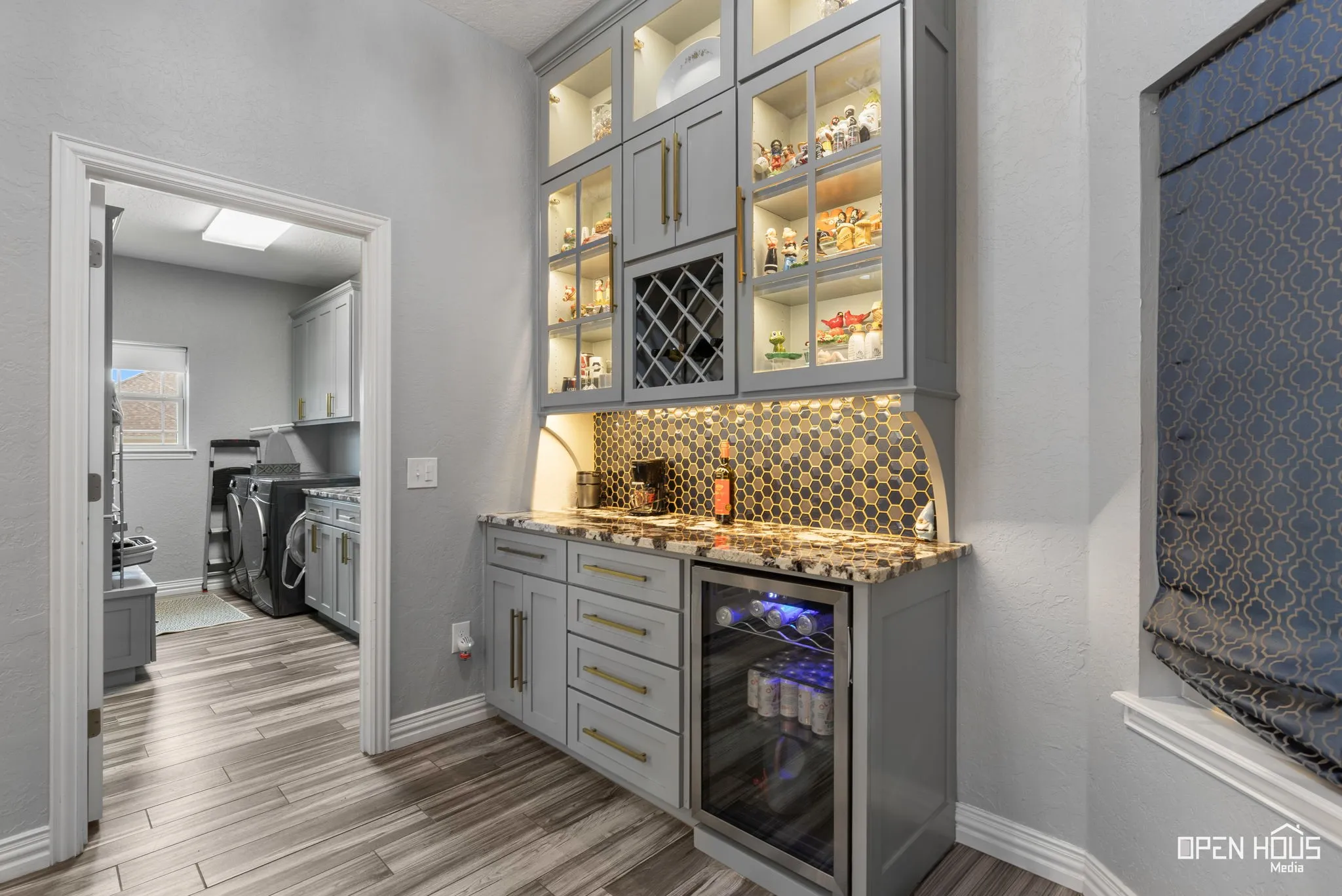 Built-in cabinetry with glass display doors, undermount lighting, stone countertop, hexagon tile backsplash, and a beverage refrigerator