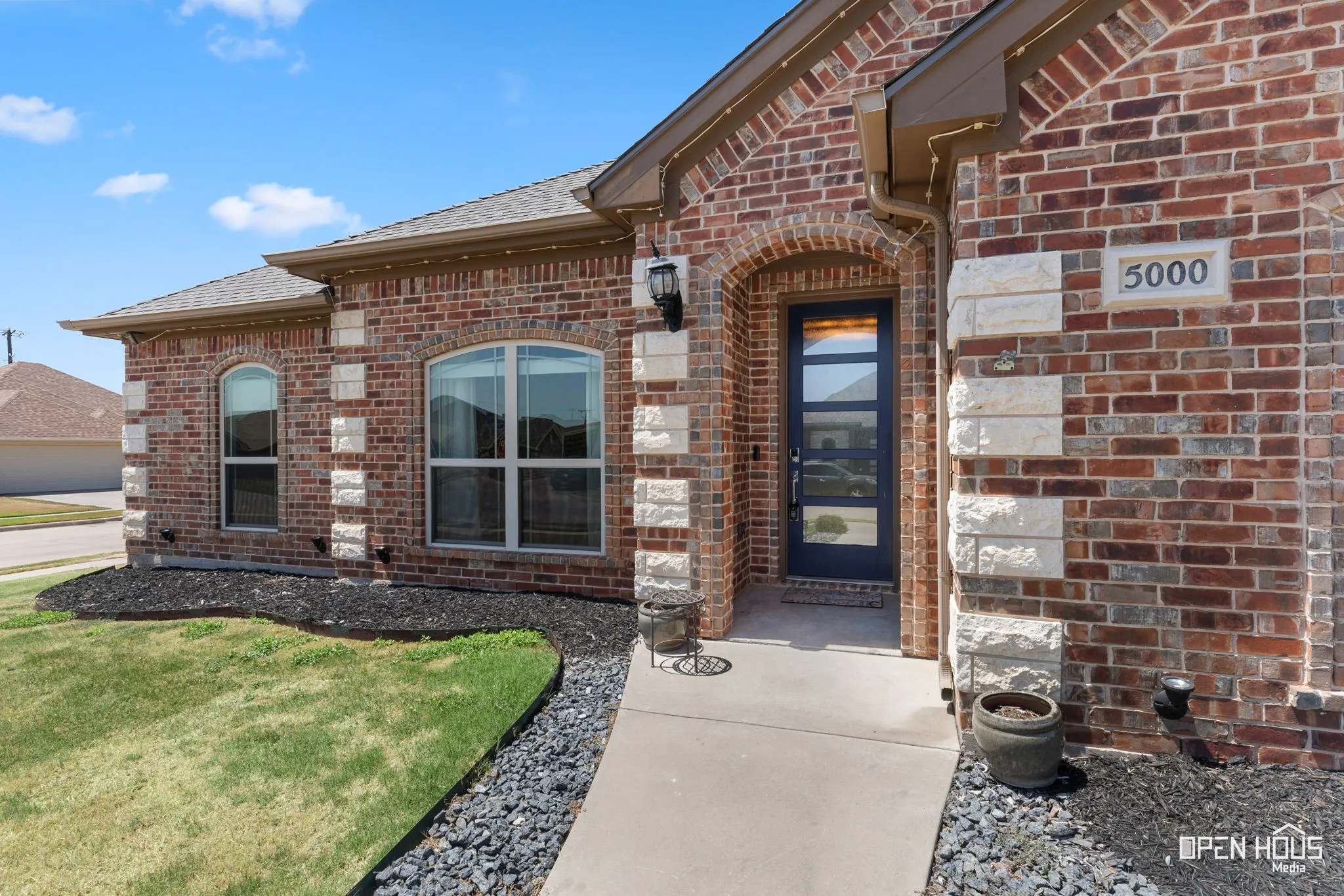 Brick exterior with stone accents, arched entry, contemporary front door, and landscape lighting