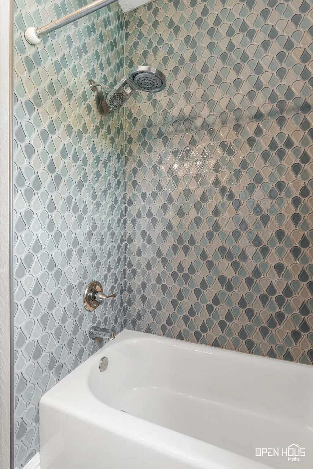 Bathtub with chrome fixtures, mosaic tile surround, and a detachable showerhead