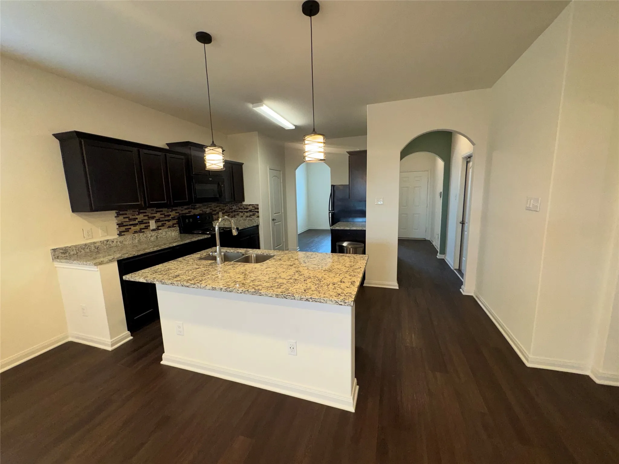 Kitchen featuring an island with a sink, dark wood-finish cabinetry, light-toned countertops, and a patterned backsplash