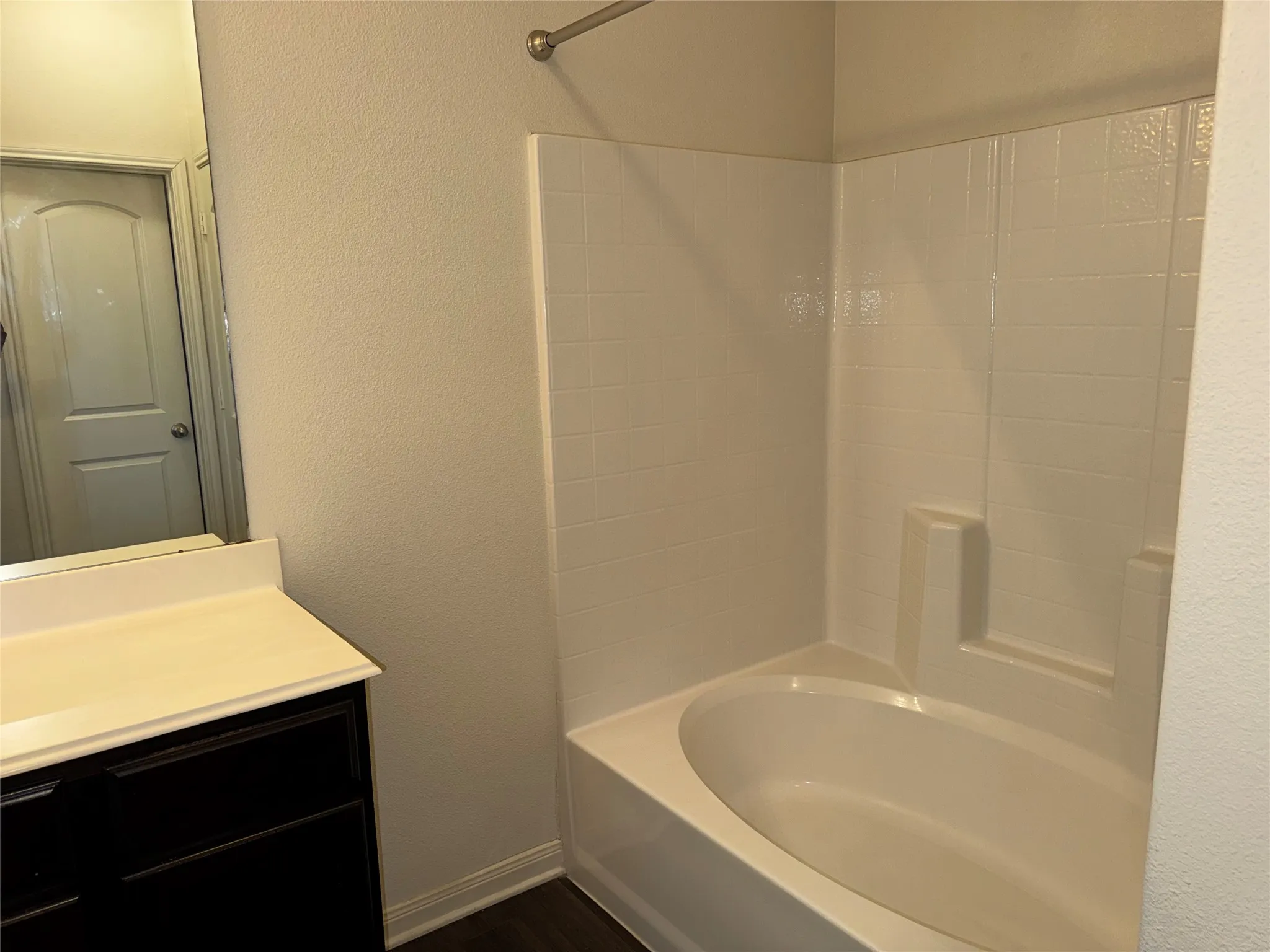 Built-in bathtub with a tile surround, dark wood-finish flooring, and a vanity with a light-toned countertop
