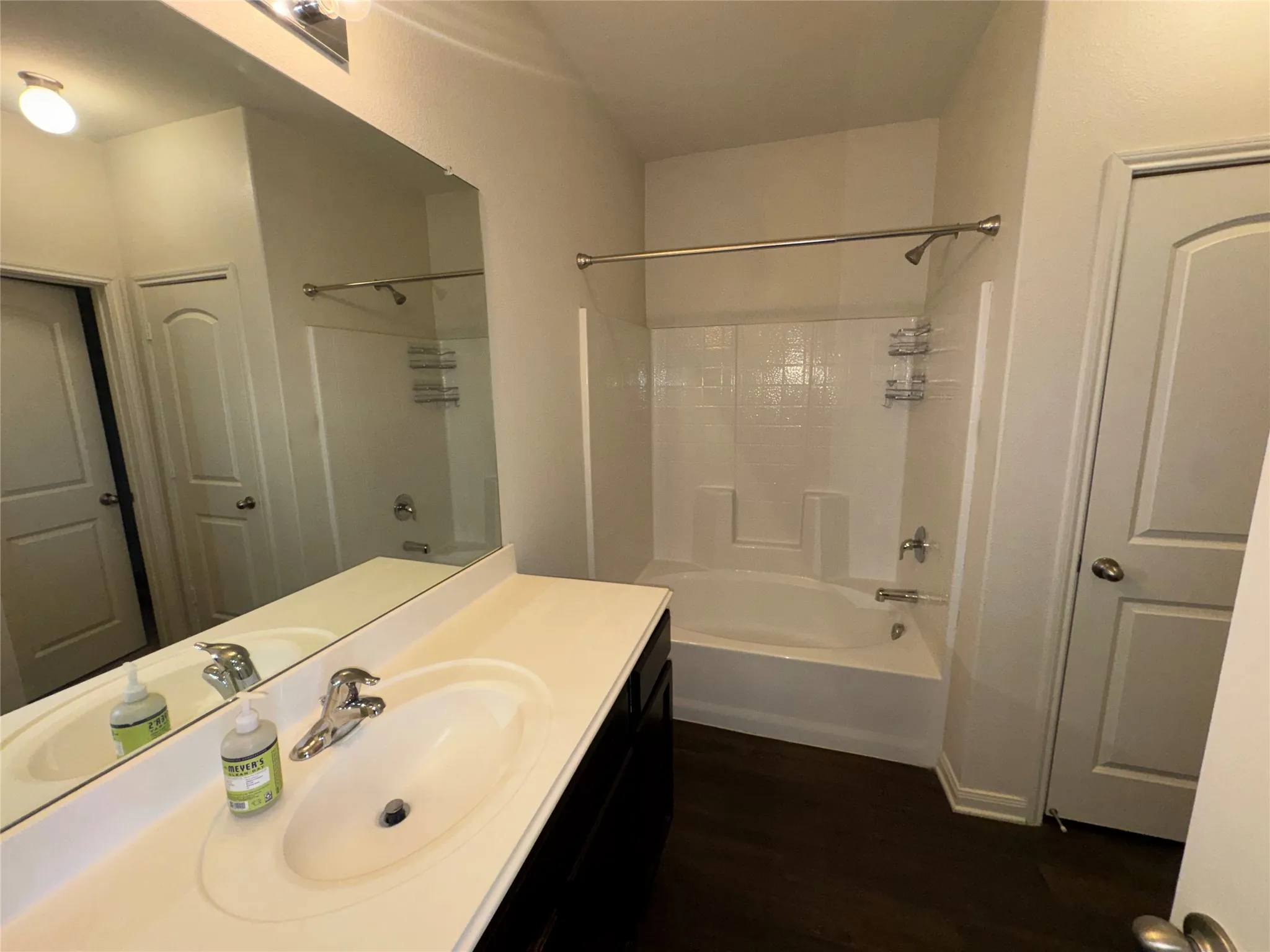 Bathroom featuring a dark wood-finish vanity, a white countertop with an integrated sink, a large wall-mounted mirror, and a white tub/shower combination with a chrome fixture