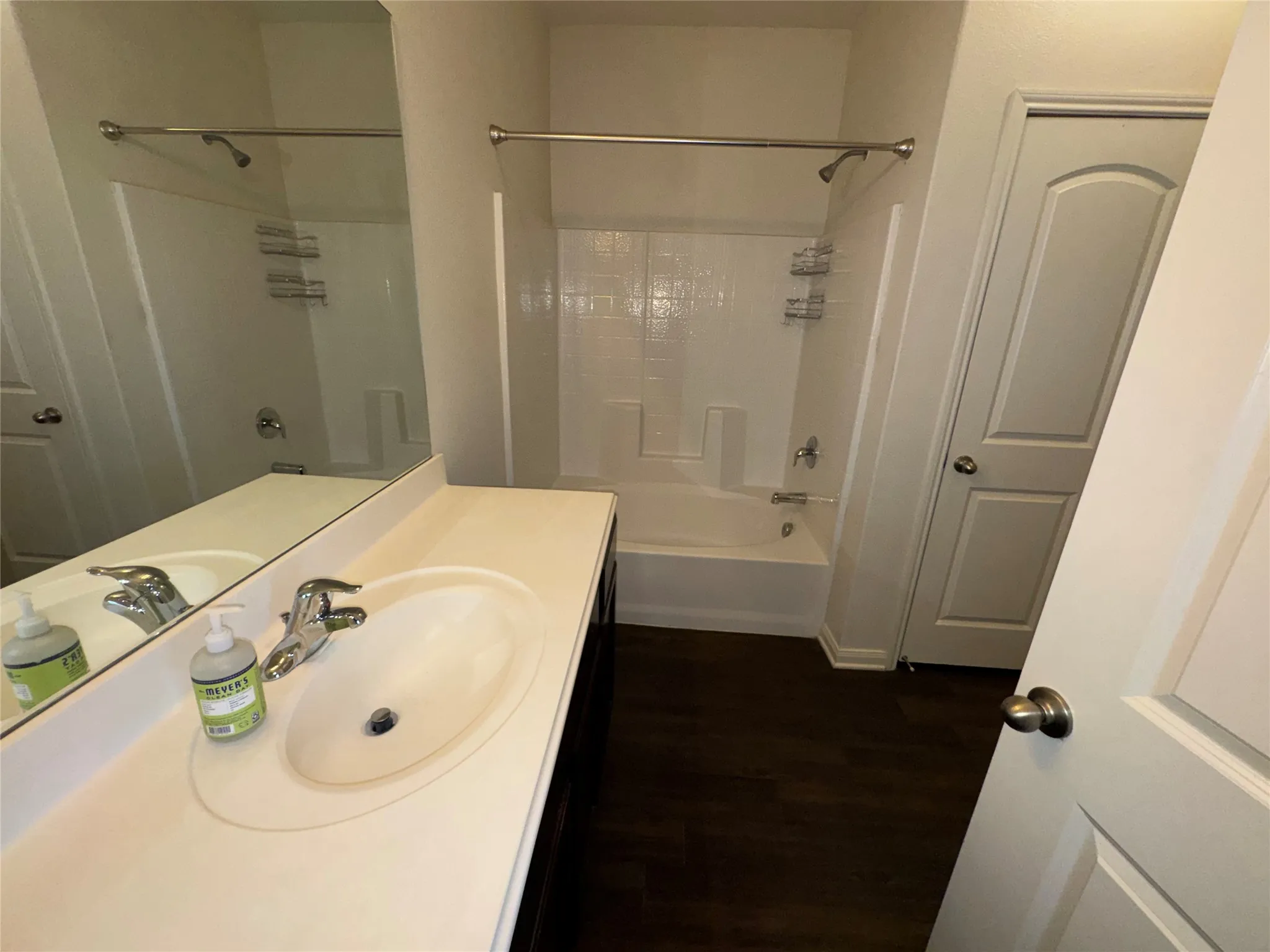 Bathroom featuring a single vanity with an integrated sink, polished chrome faucet, a full-width mirror, and a white bathtub with a shower