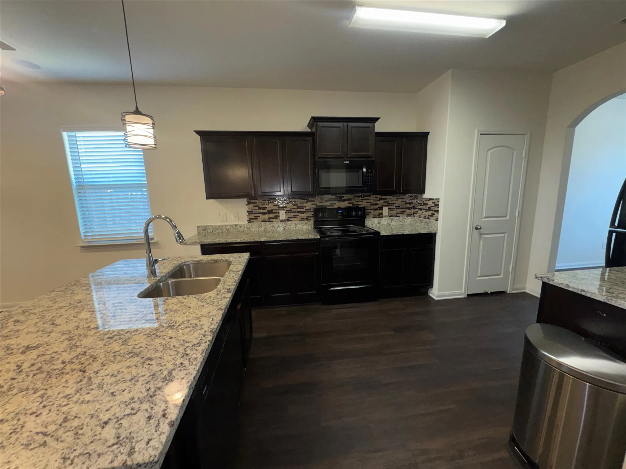 Kitchen featuring dark wood-finish cabinetry, light-toned countertops, tile backsplash, and dark wood-finish flooring
