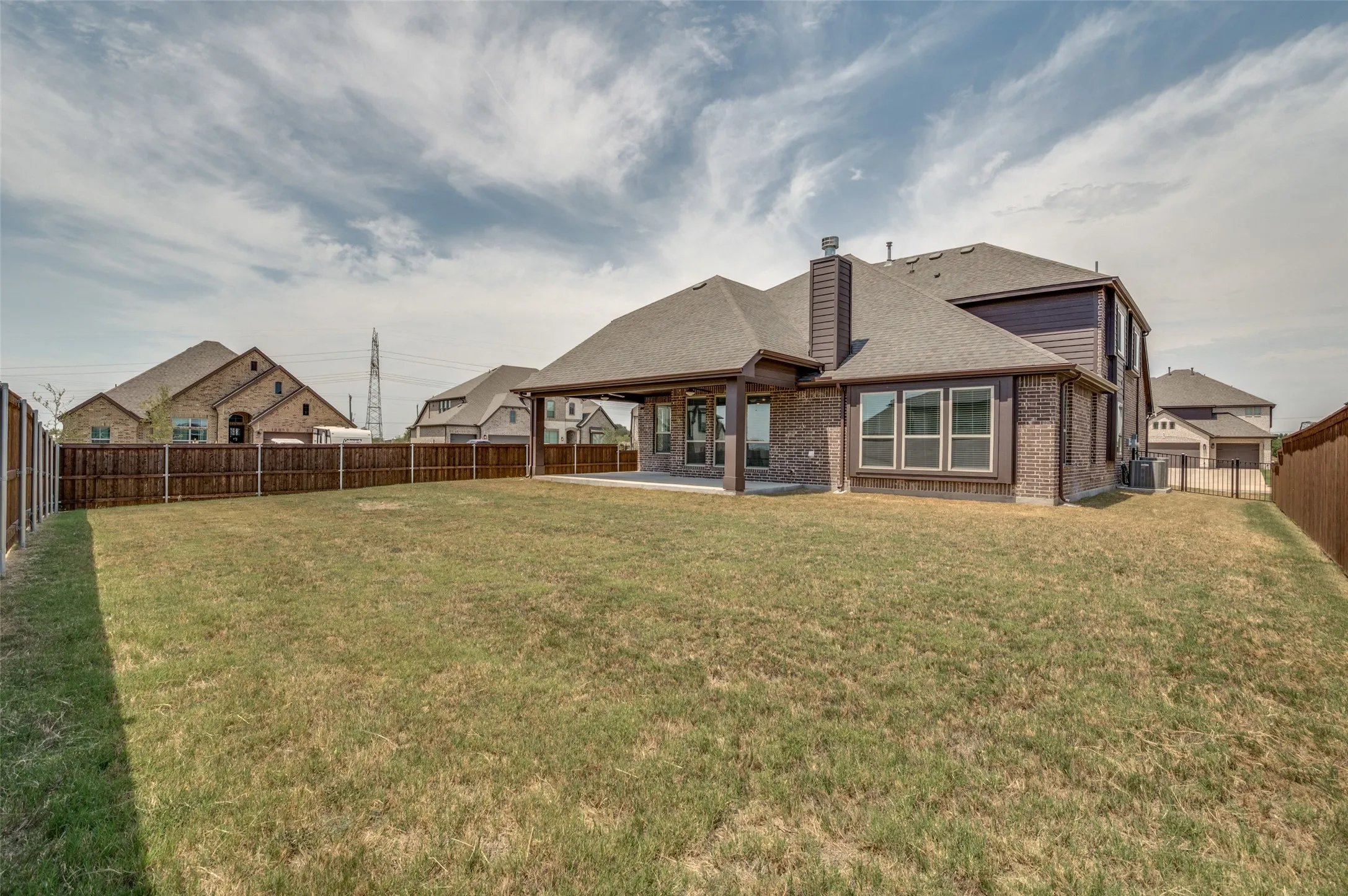 Expansive backyard with a covered patio, brick exterior, and a privacy fence