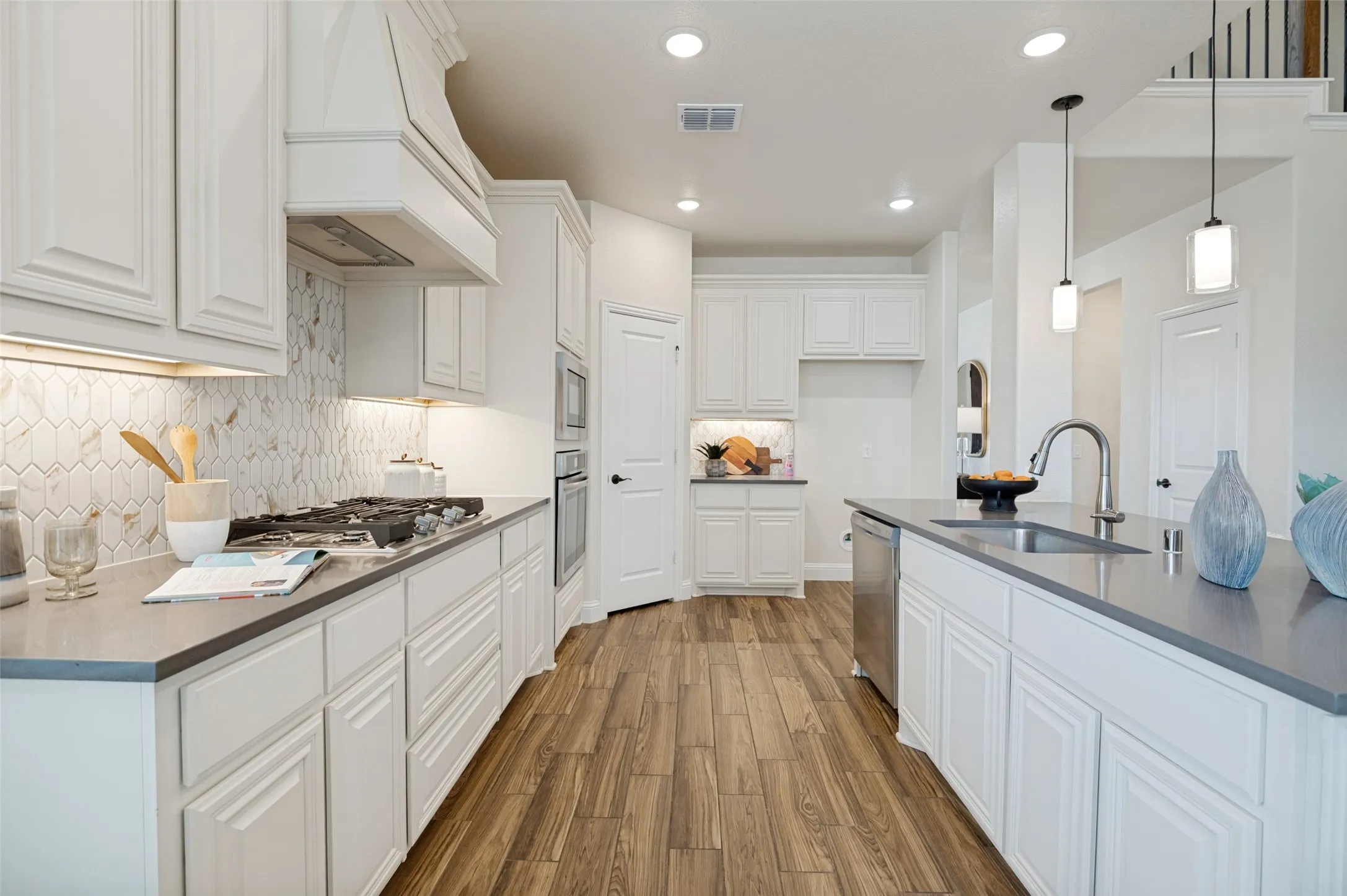 Kitchen featuring white cabinetry, gray countertops, wood-finish flooring, a tile backsplash, and stainless steel appliances
