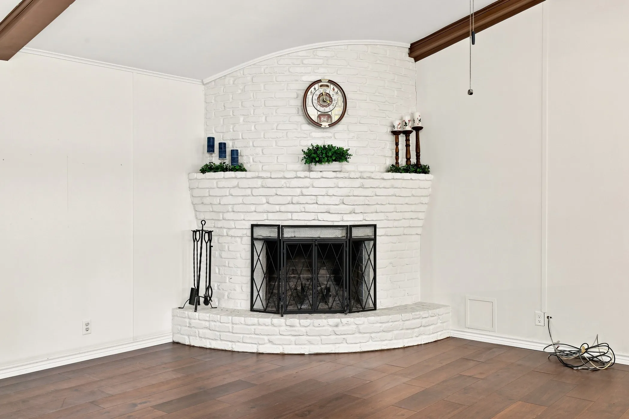 Corner fireplace with white painted brick surround and hearth, wood-finish flooring, and exposed wood beam
