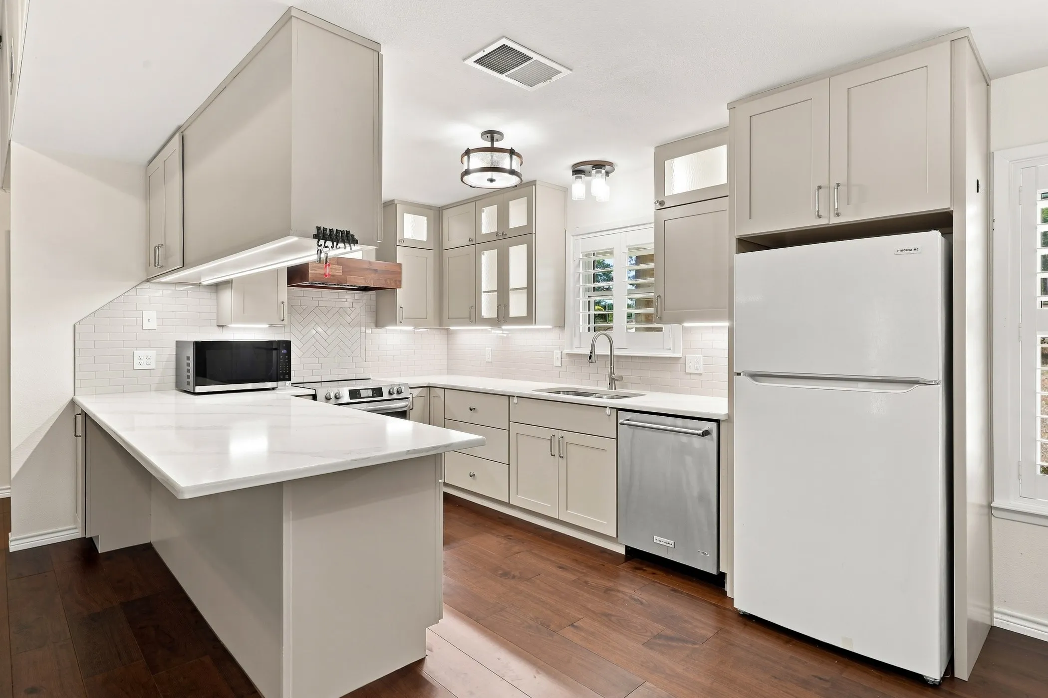 Kitchen featuring light-toned cabinetry, white countertops, stainless steel appliances, and dark wood-finish flooring