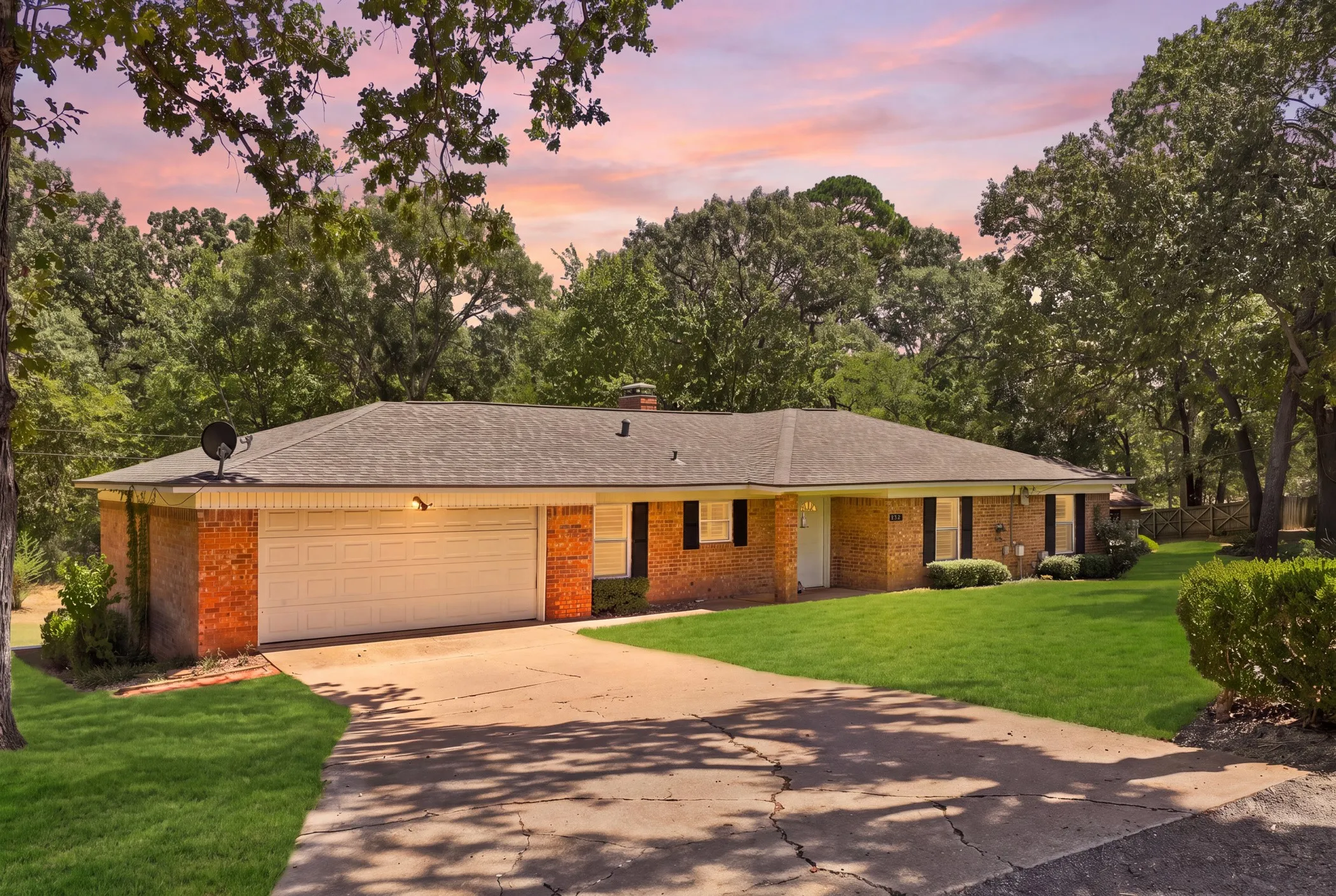 Brick facade residence with an attached two-car garage, mature landscaping, a paved driveway, and a shingle roof