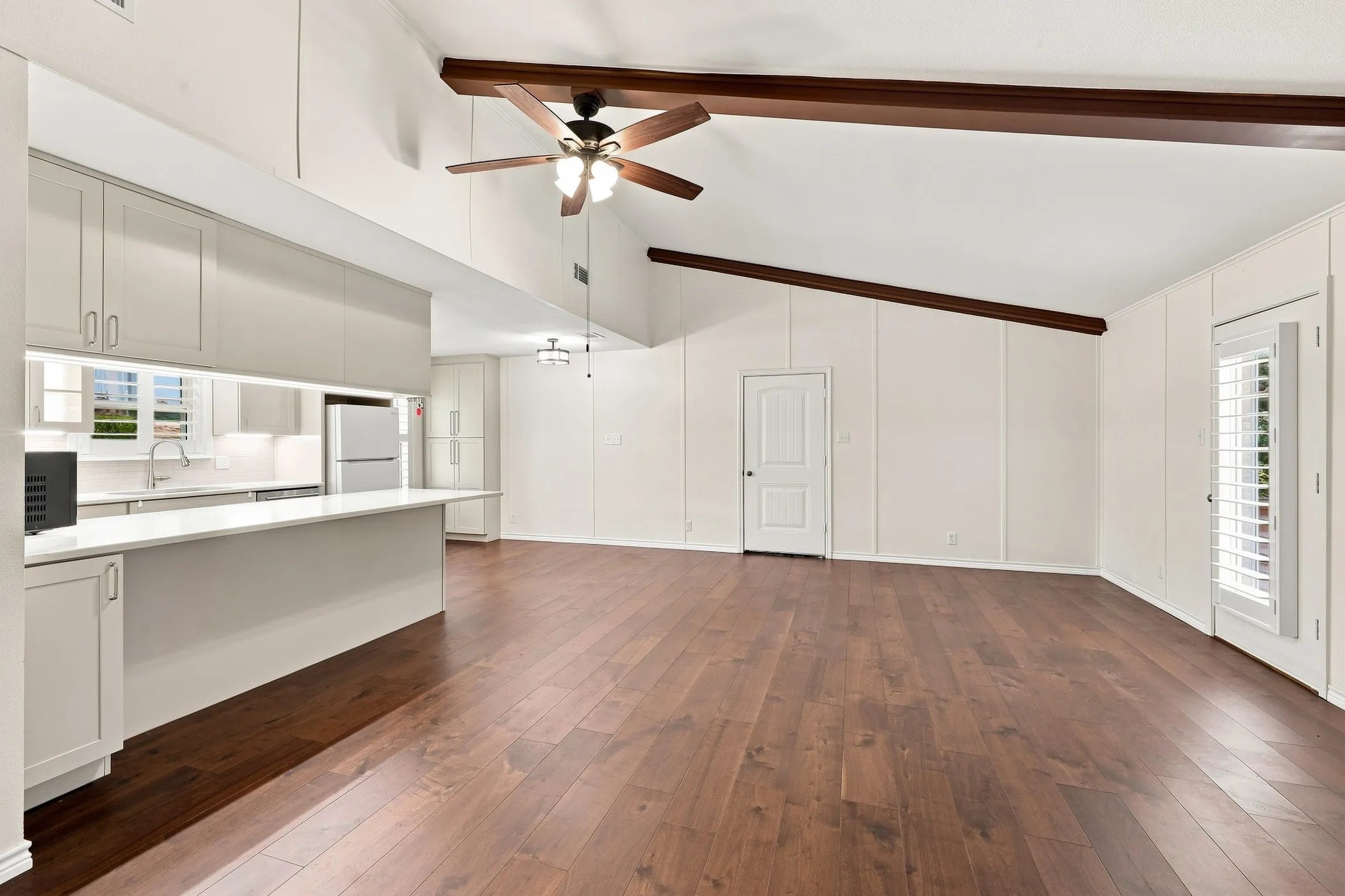 Vaulted ceilings with exposed wood beams, wood-finish flooring, white cabinetry, integrated kitchen lighting, and a kitchen island with a breakfast bar