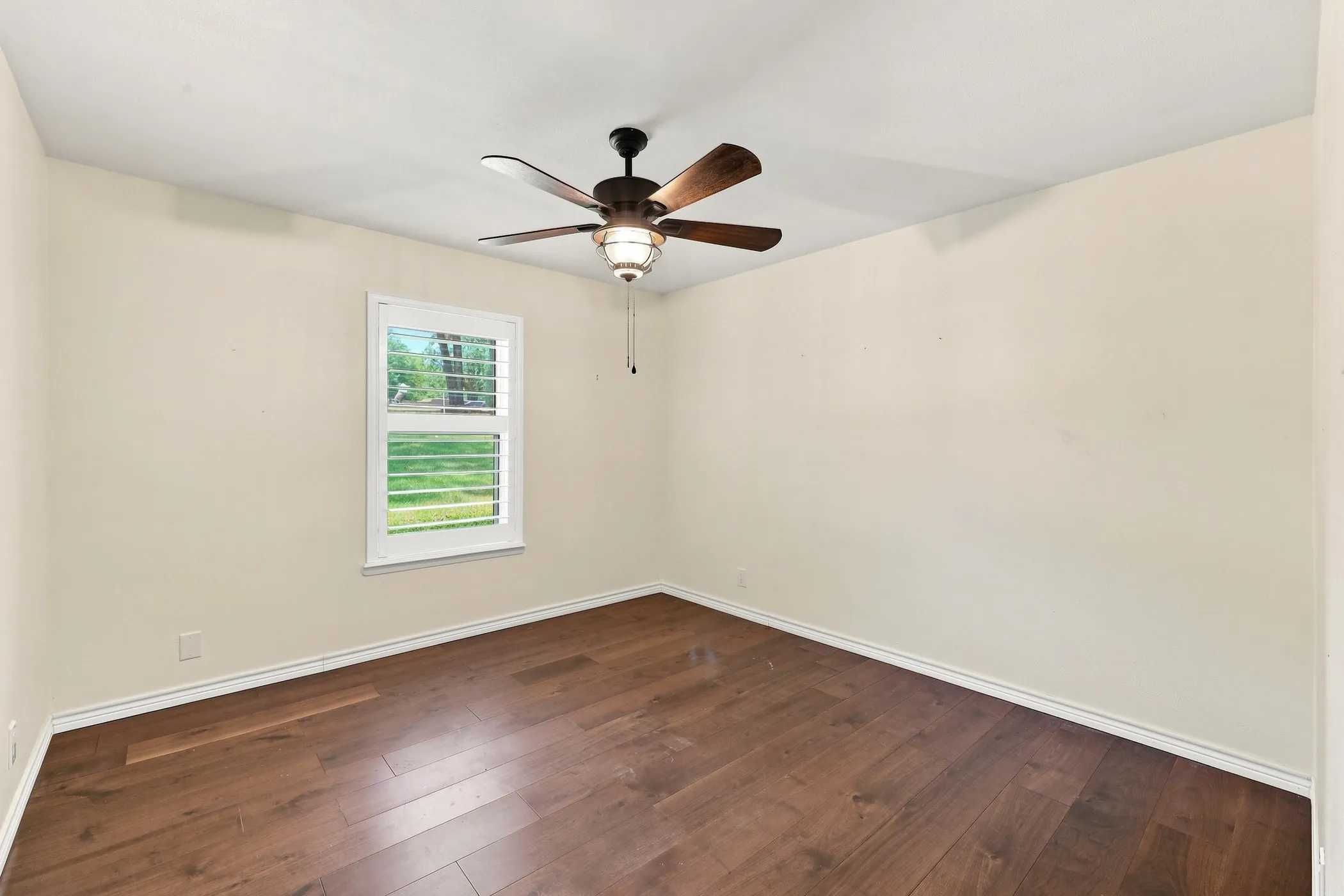Wood-finish flooring, ceiling fan with integrated lighting, window with plantation shutters, and light-toned walls