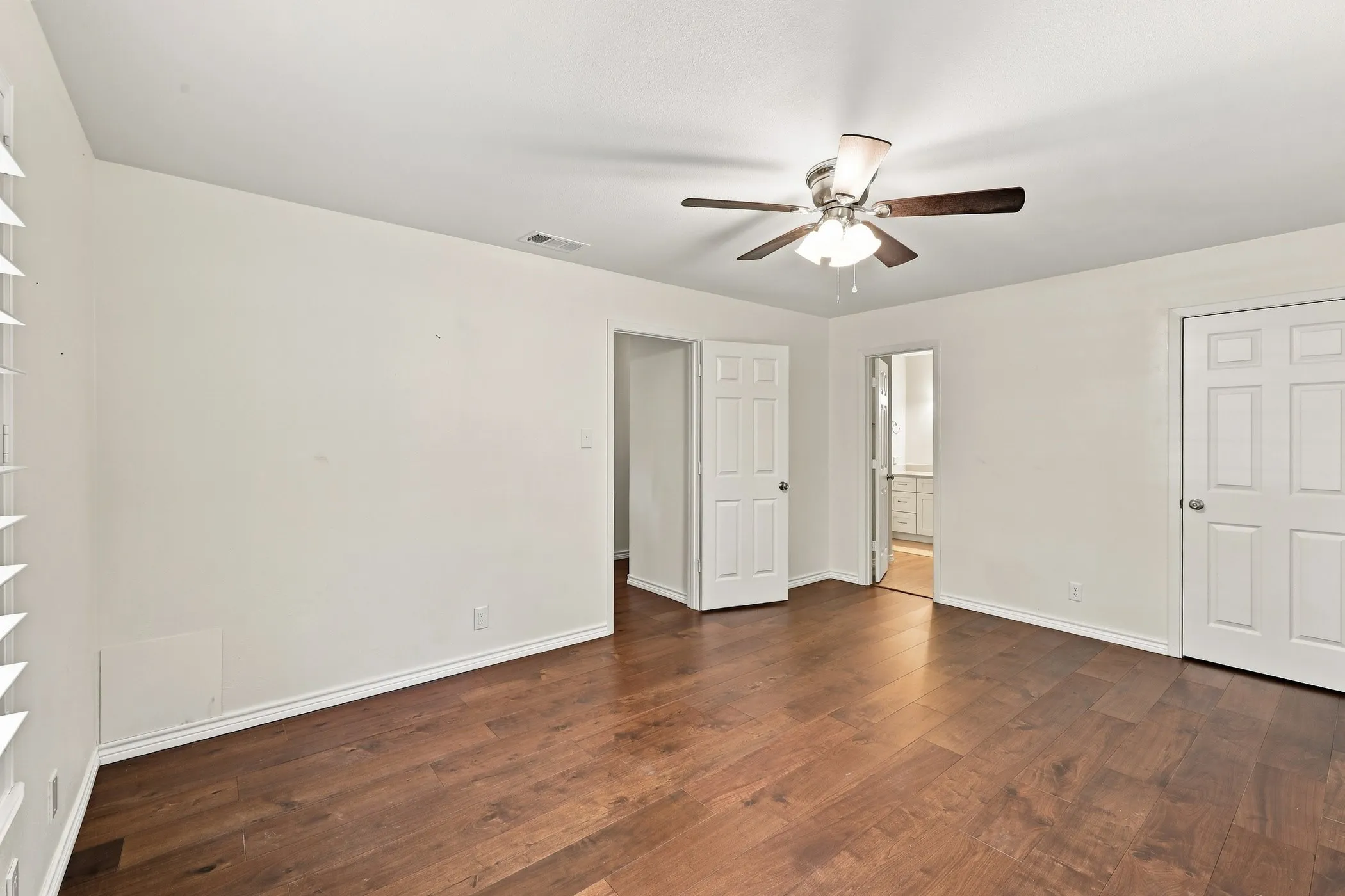Wood-finish flooring, ceiling fan with light fixture, white interior doors, and window with white blinds
