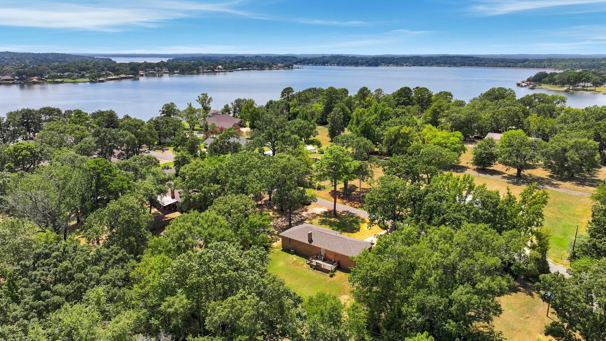 Expansive lakefront property featuring a brick exterior, mature trees, and a spacious lot with water frontage