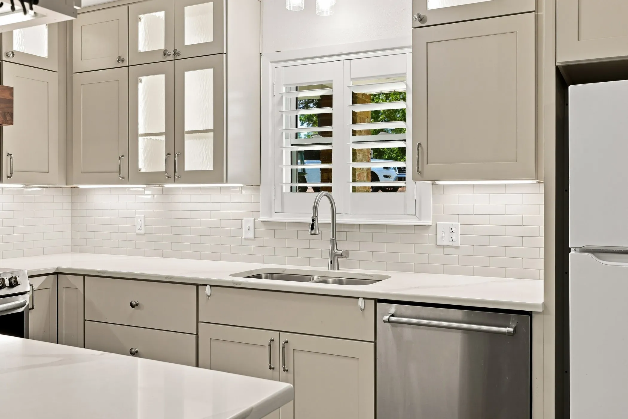Kitchen featuring light-toned cabinetry, stainless steel sink, subway tile backsplash, and under-cabinet lighting