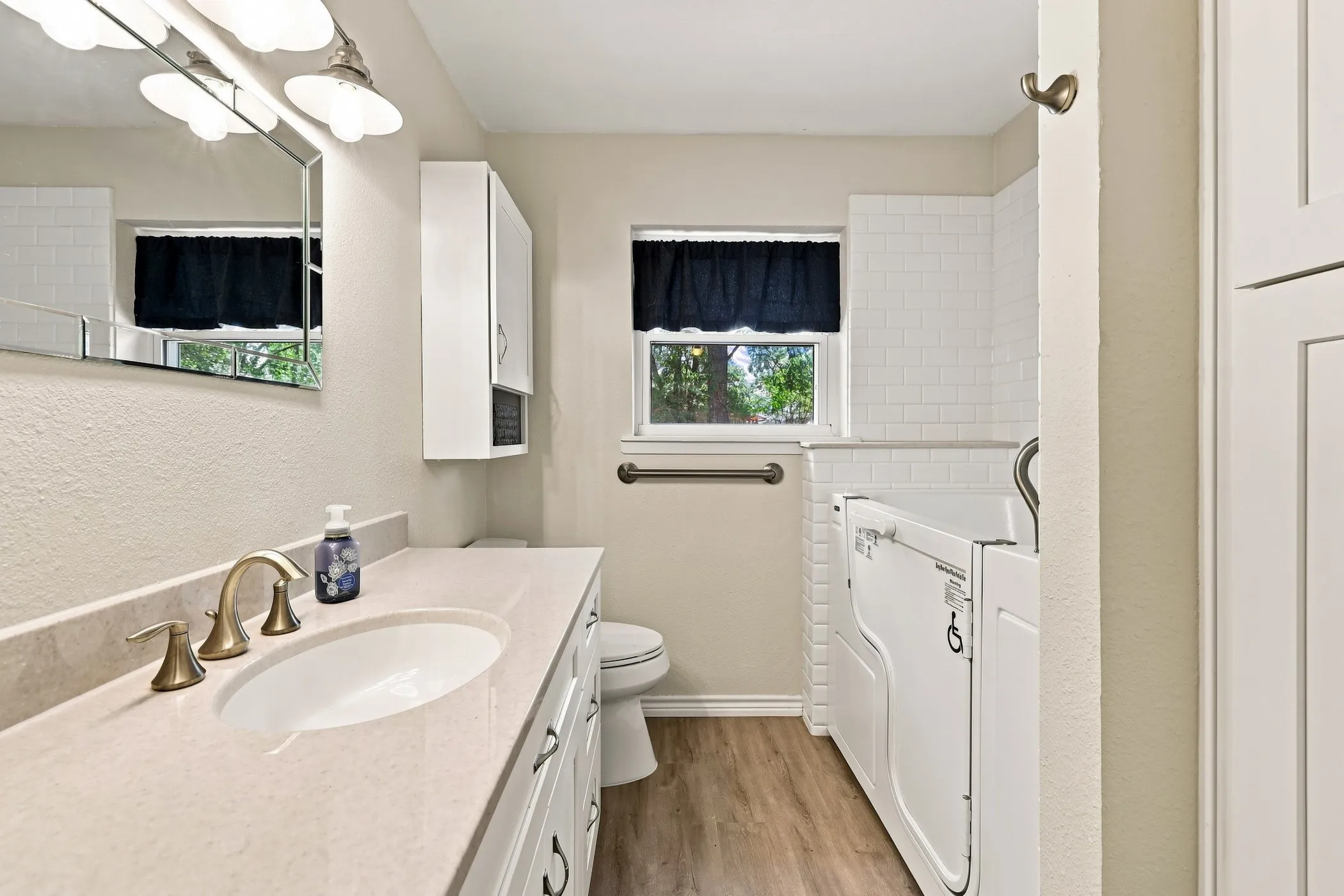 Bathroom featuring a vanity with an integrated sink, a walk-in tub, and wood-finish flooring
