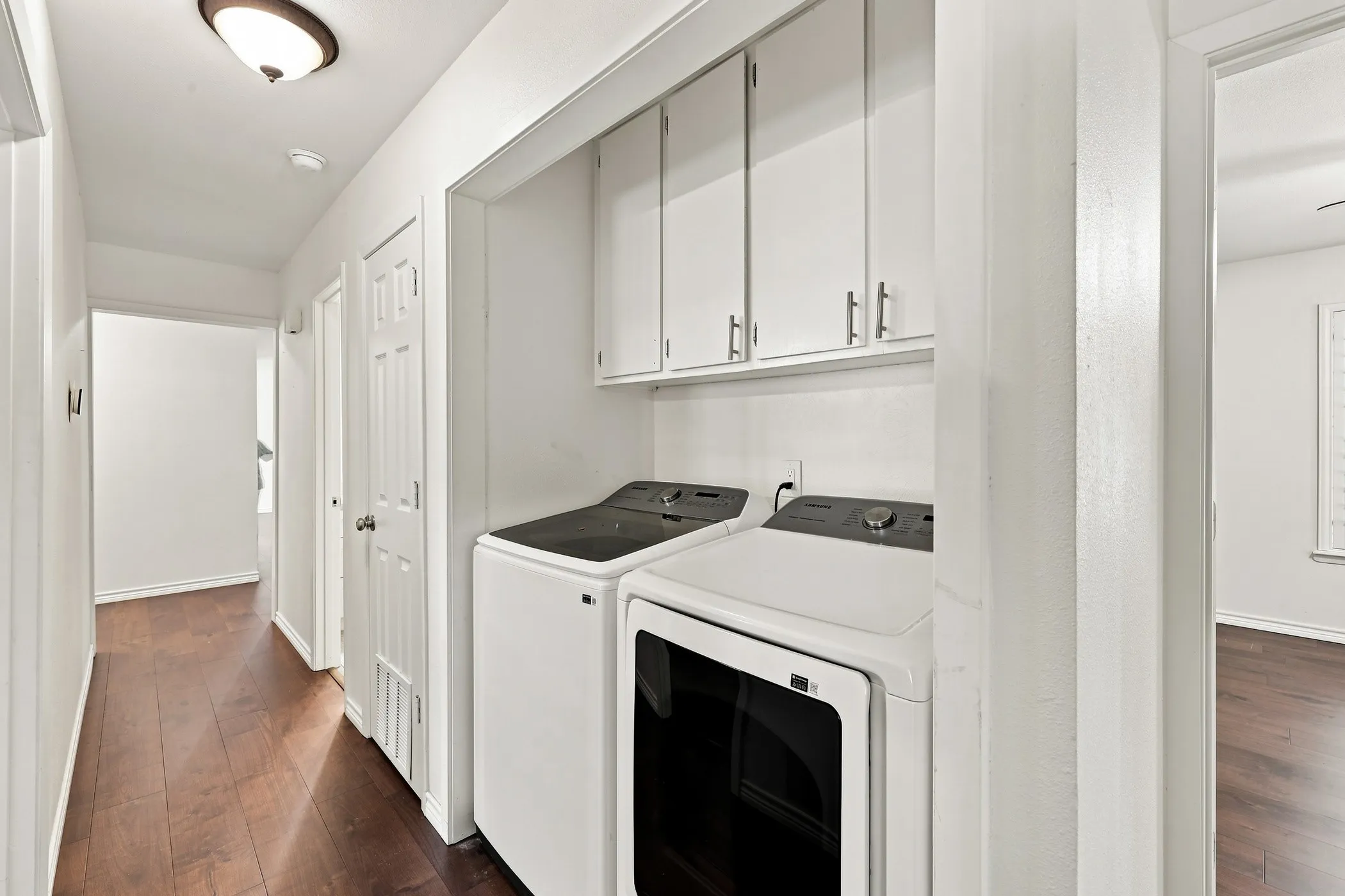 Laundry area with overhead white cabinetry, wood-finish flooring, and white walls