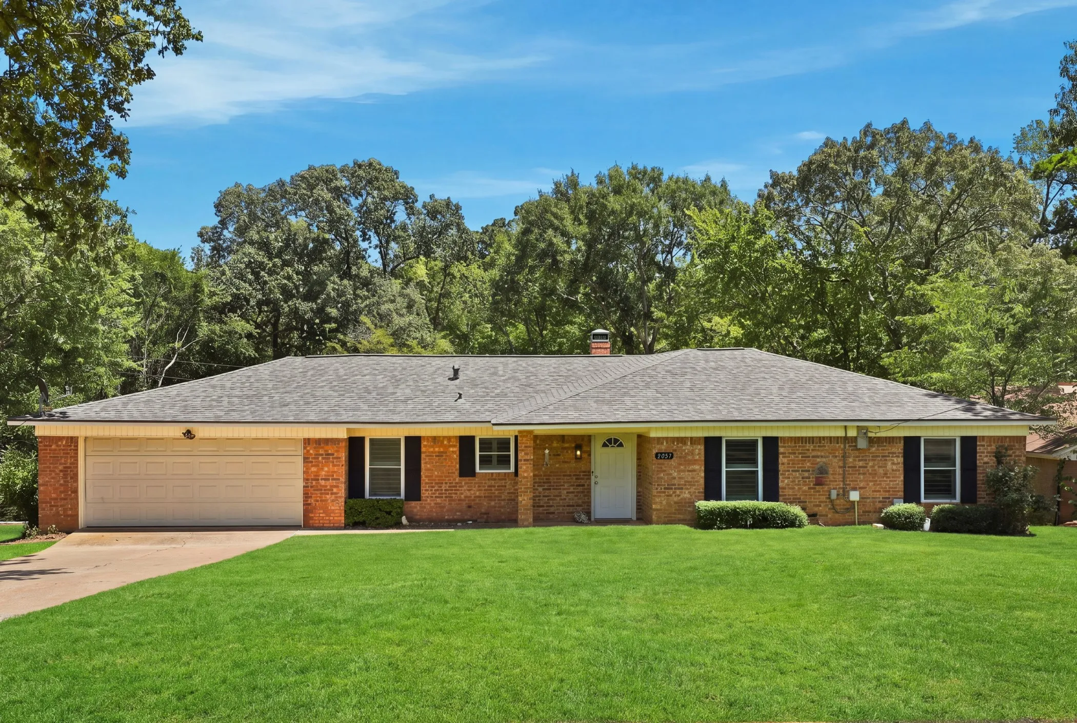 Brick exterior with a shingle roof, attached garage, and a lush green lawn