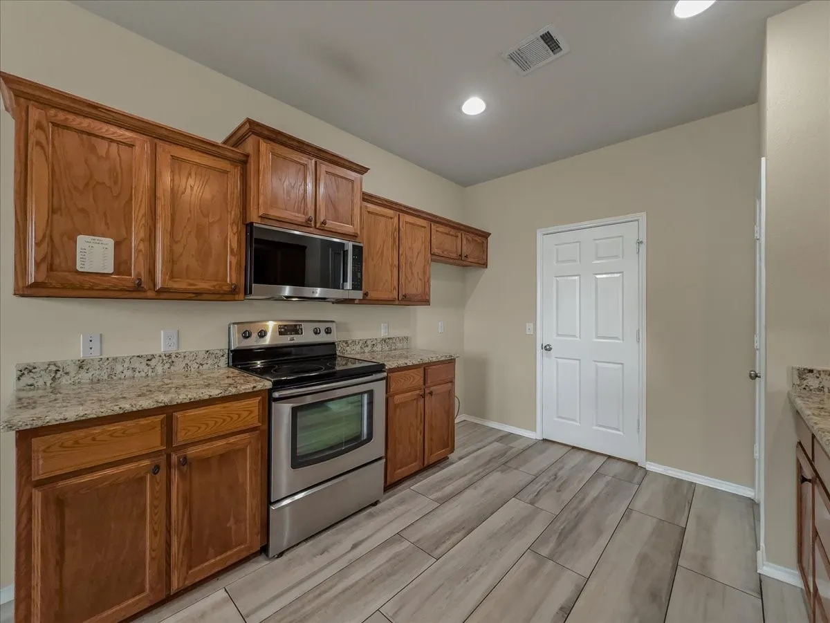 Wood-finish flooring, recessed lighting, wood cabinetry, stone countertops, and stainless steel appliances