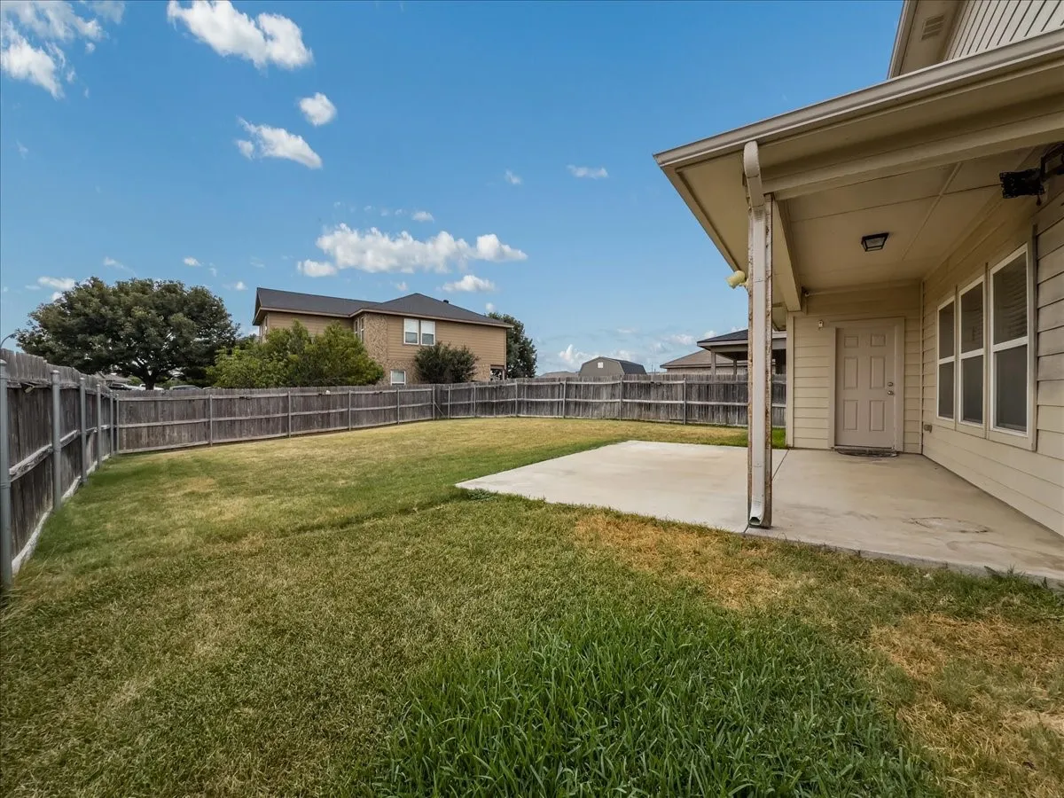 Expansive fenced backyard featuring a concrete patio, wood privacy fencing, and a stucco exterior