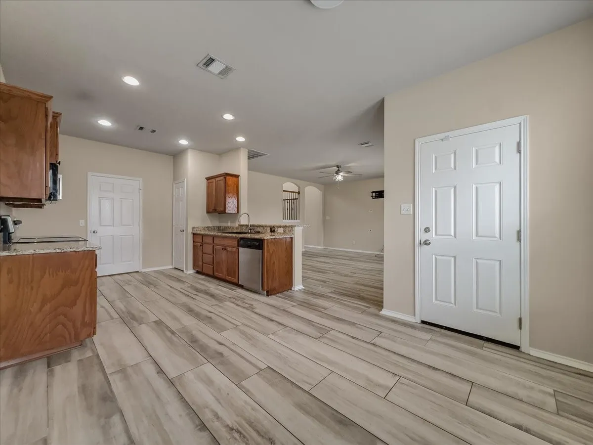 Kitchen with wood-finish flooring, recessed lighting, wood cabinetry, granite-style countertops, and stainless steel dishwasher