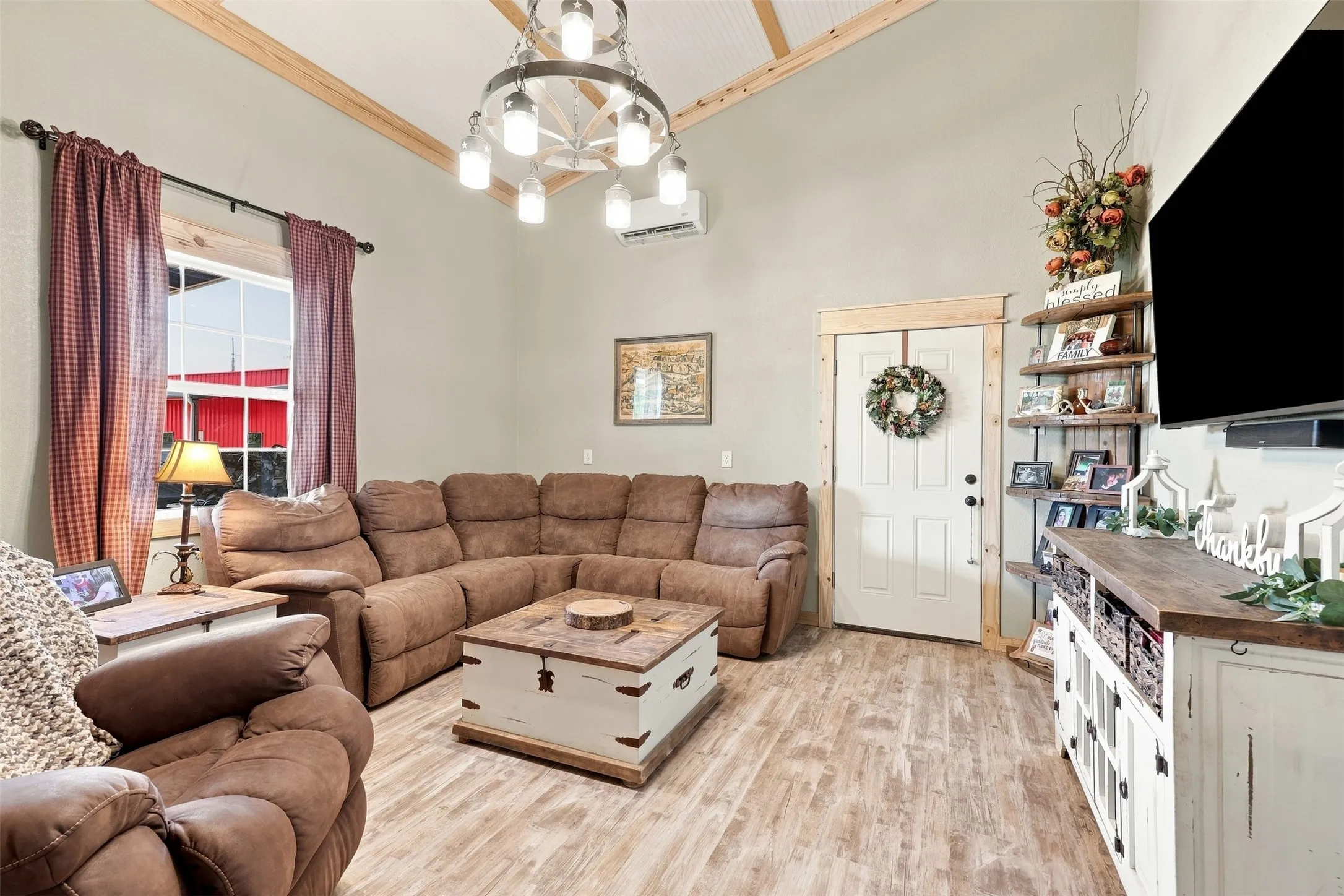 Vaulted ceiling with exposed wood beams, wood-finish flooring, white paneled door with wood trim, built-in corner shelving, and a decorative chandelier
