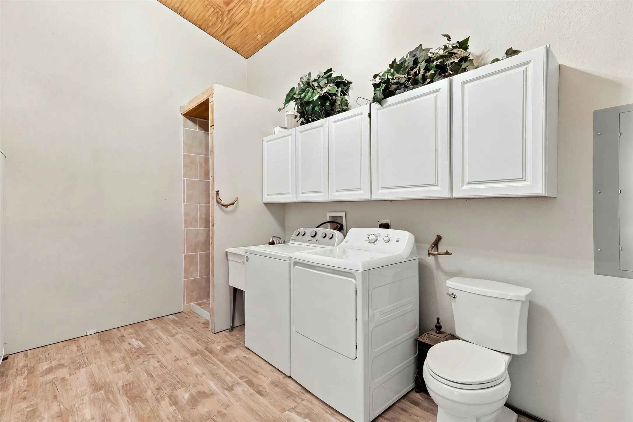 Vaulted wood-finish ceiling, wood-finish flooring, white cabinetry, utility sink, and a toilet
