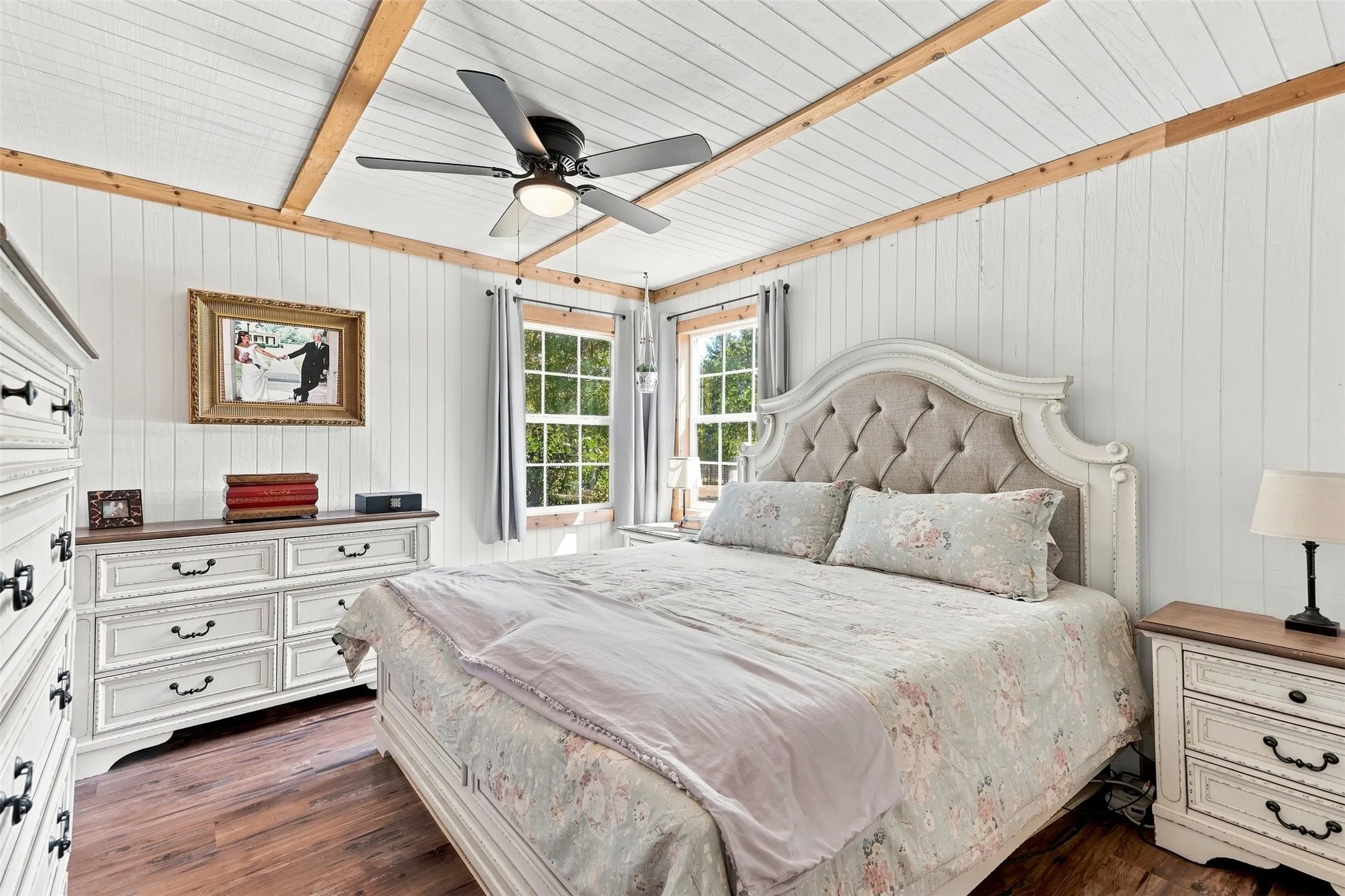 Wood-finish flooring with white vertical wall paneling, white planked ceiling, and exposed wood beams