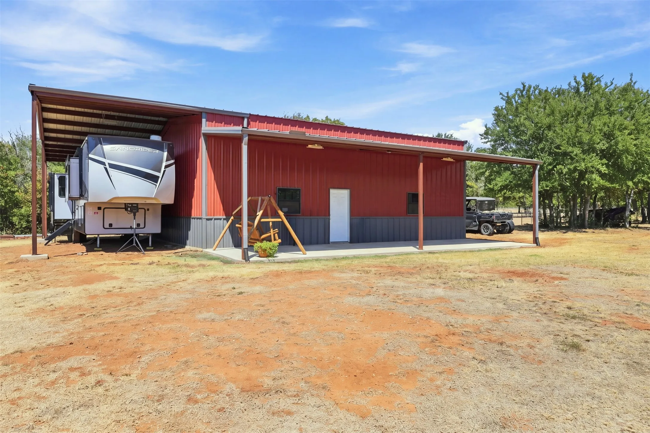 Red and gray metal building with a white entry door, an attached covered carport, and an extended covered patio