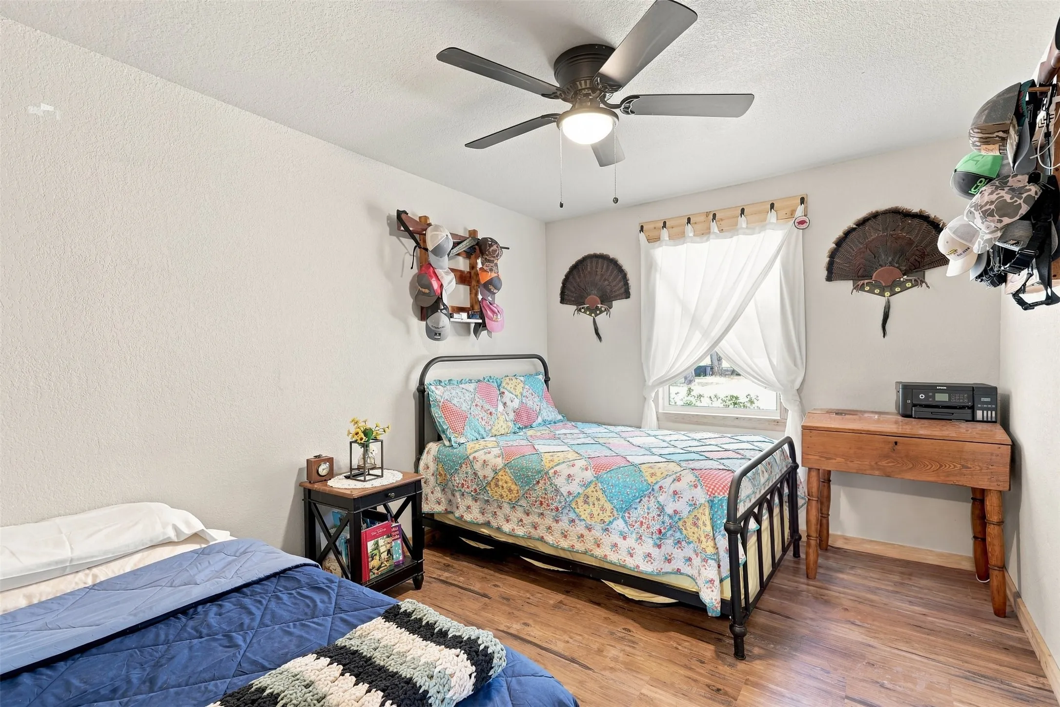 Textured walls, wood-finish flooring, ceiling fan with integrated lighting, and a window with curtain rods