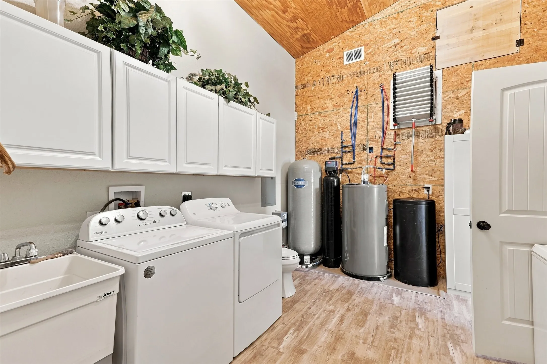 Utility room featuring wood-finish flooring, white cabinetry, a utility sink, and exposed structural elements