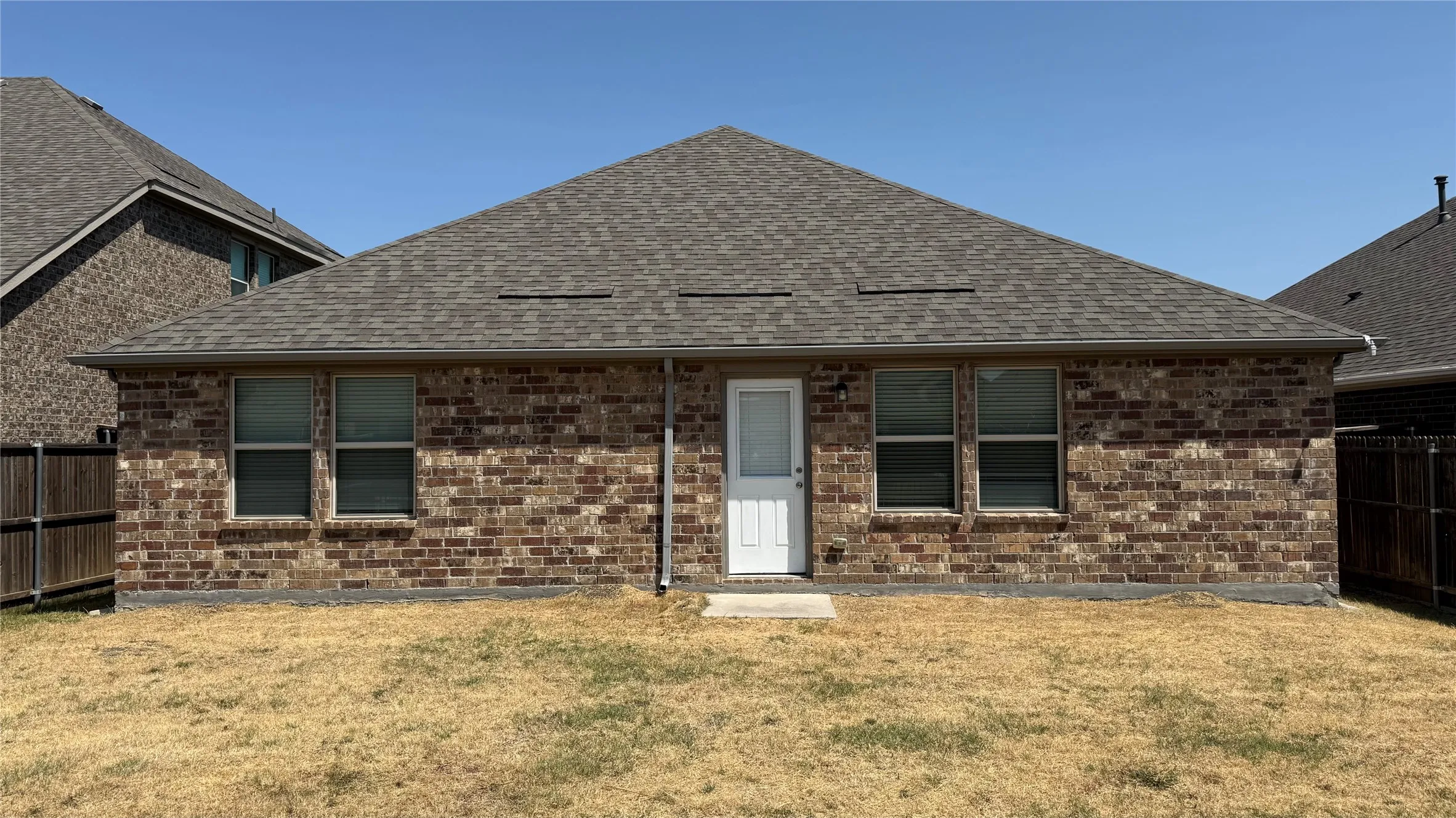 Brick exterior with a shingle roof, white back door, and multiple windows